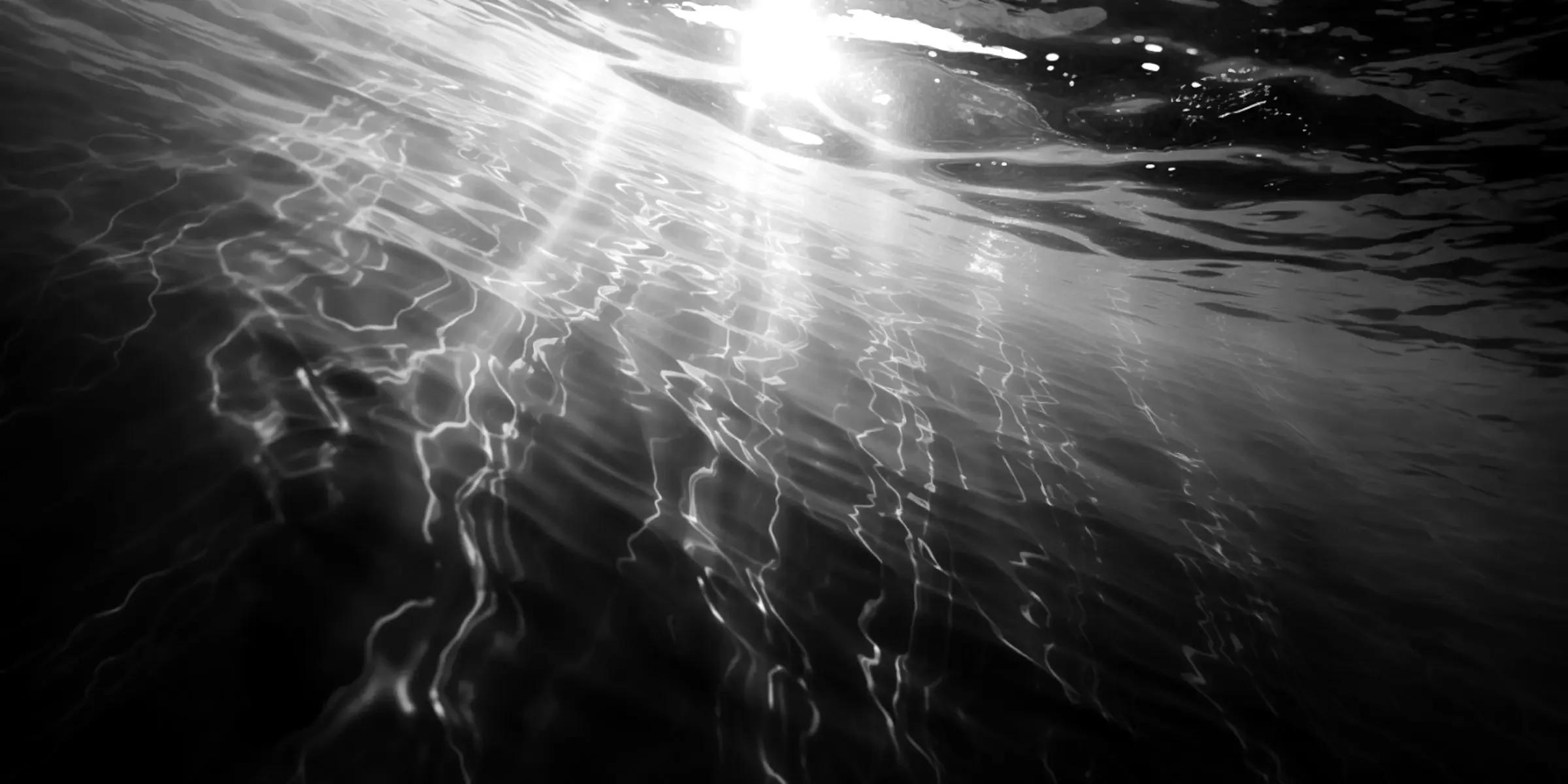 Surface de l'eau avec des reflets et des éclats de lumière, en noir et blanc.