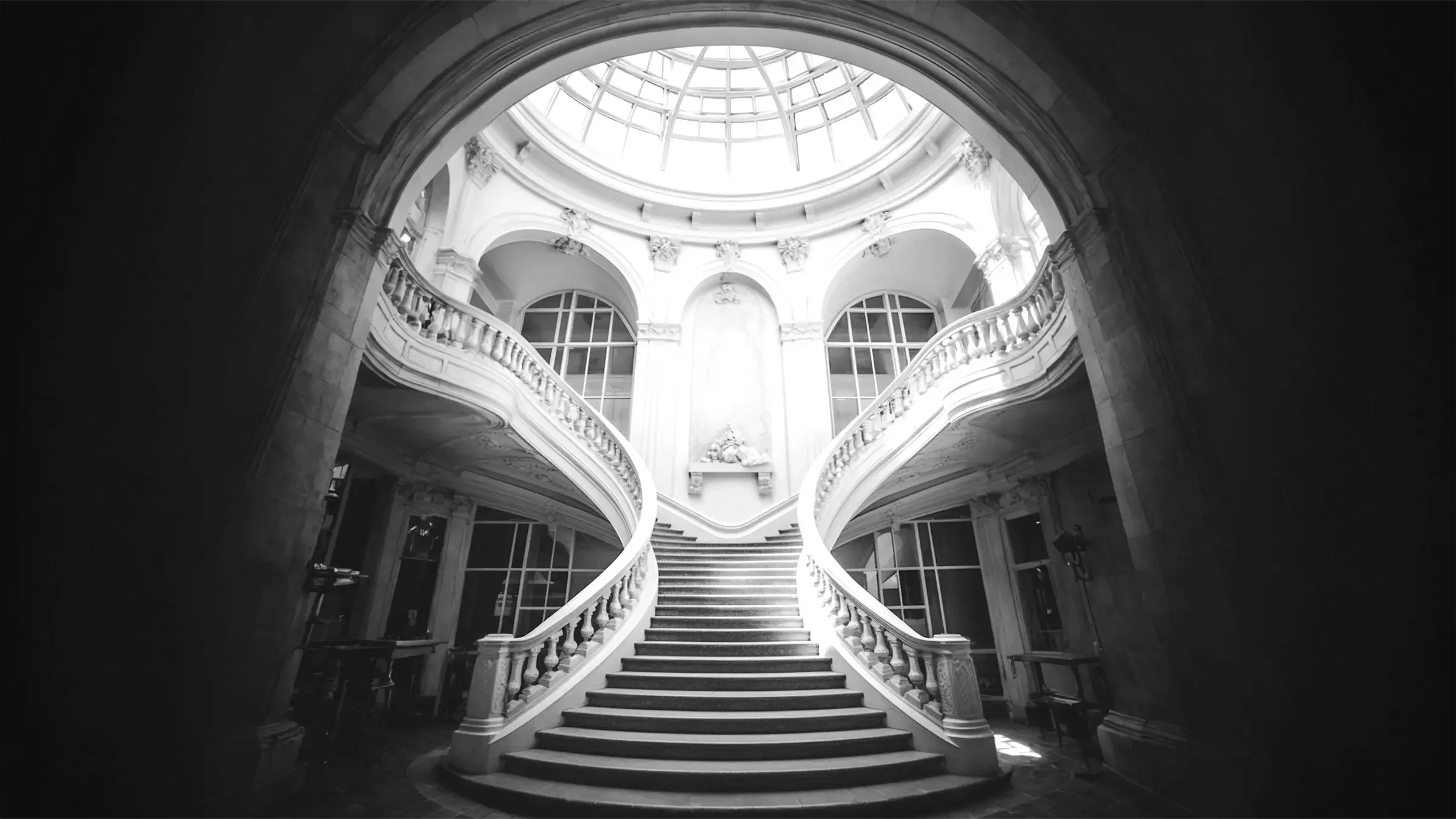 Escalier monumental à double volée dans un bâtiment institutionnel, architecture classique, lumière zénithale soulignant un cadre solennel et cérémoniel.