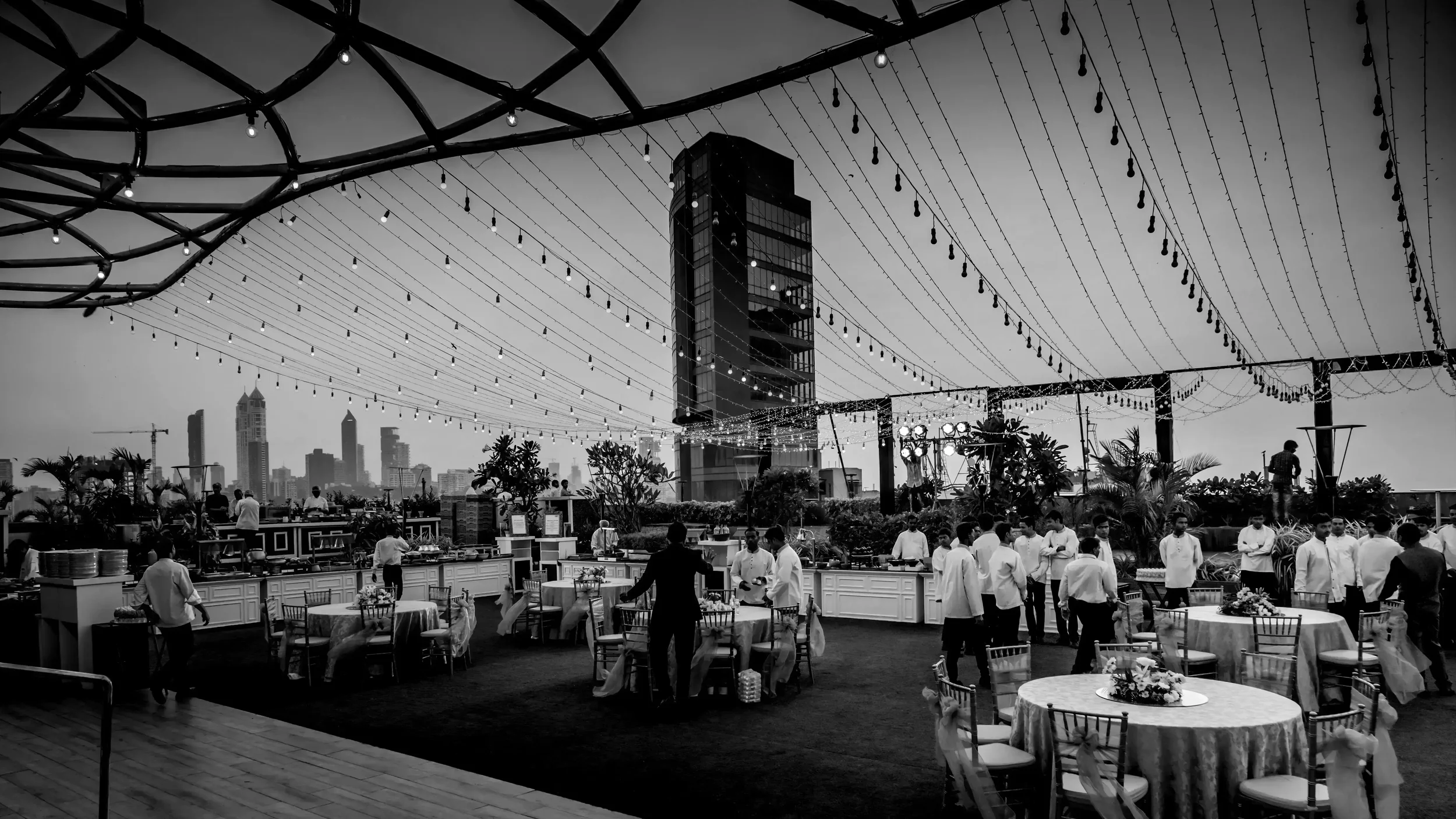Réception professionnelle en extérieur sur un rooftop, avec tables dressées, personnel en service et éclairage suspendu