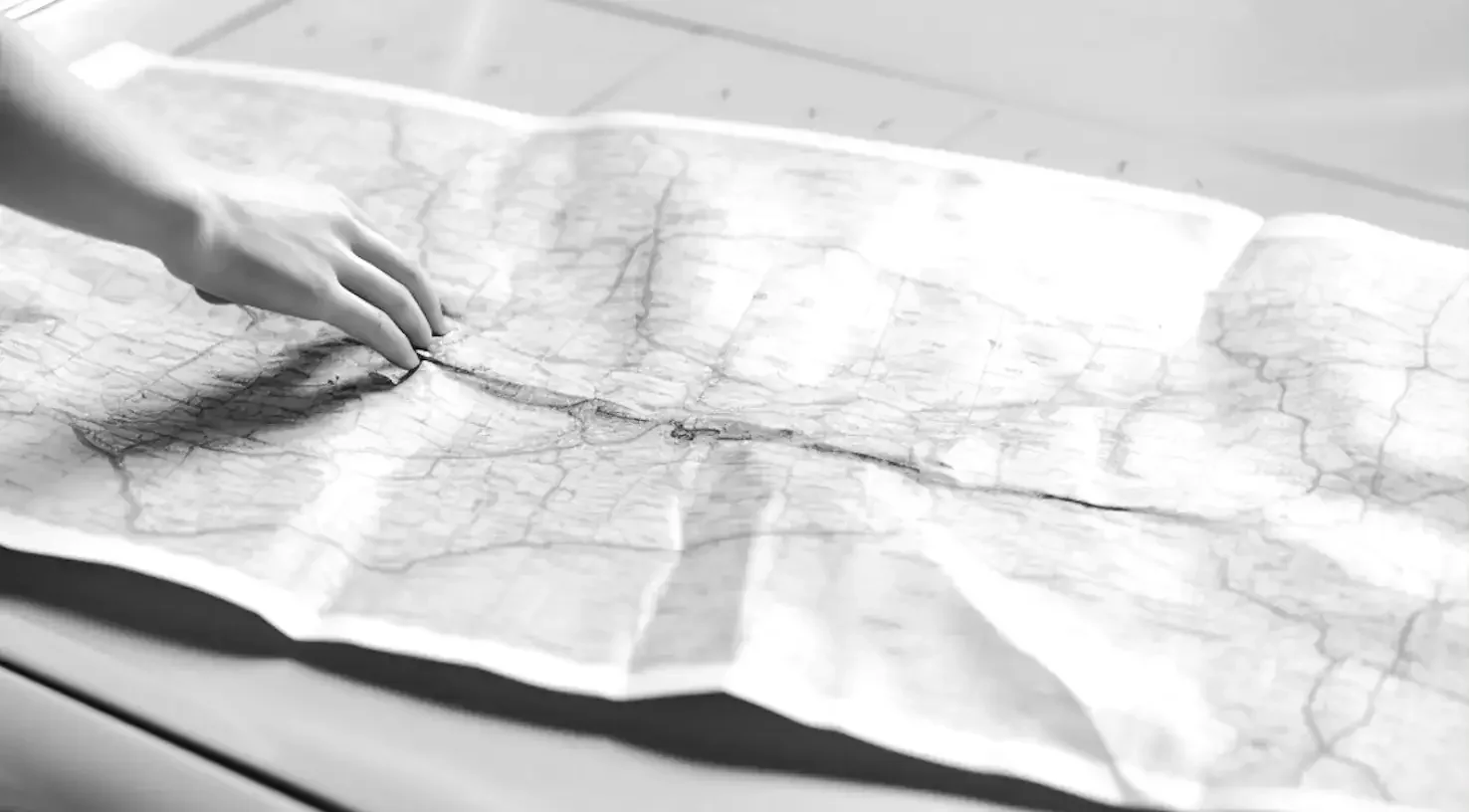 Main indiquant une route sur une carte en noir et blanc, illustrant la prospection stratégique, l’identification d’opportunités et le business development international – Fulgurance.