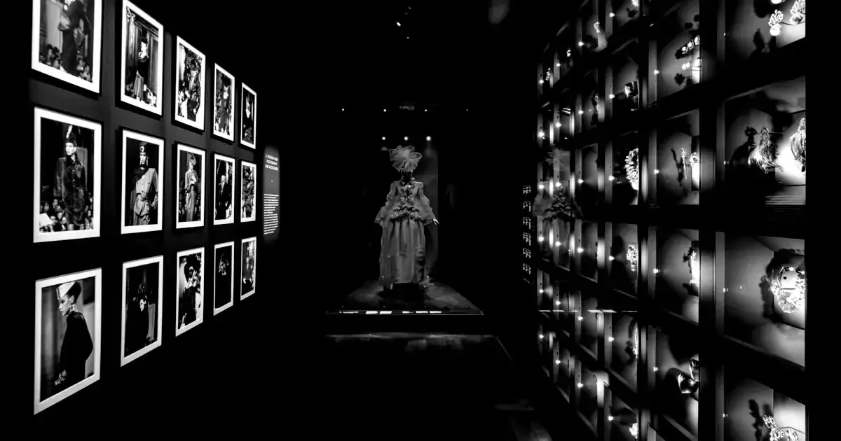 Robe de haute couture exposée dans un écrin muséal, entourée d’archives photographiques, illustrant l’héritage et la rencontre entre savoir-faire artisanal et excellence culturelle – Fulgurance.