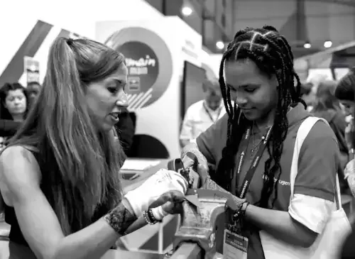 Deux femmes en conversation dans un environnement professionnel, l'une montre quelque chose avec un outil à l'autre, tous deux portant un badge d'identification.