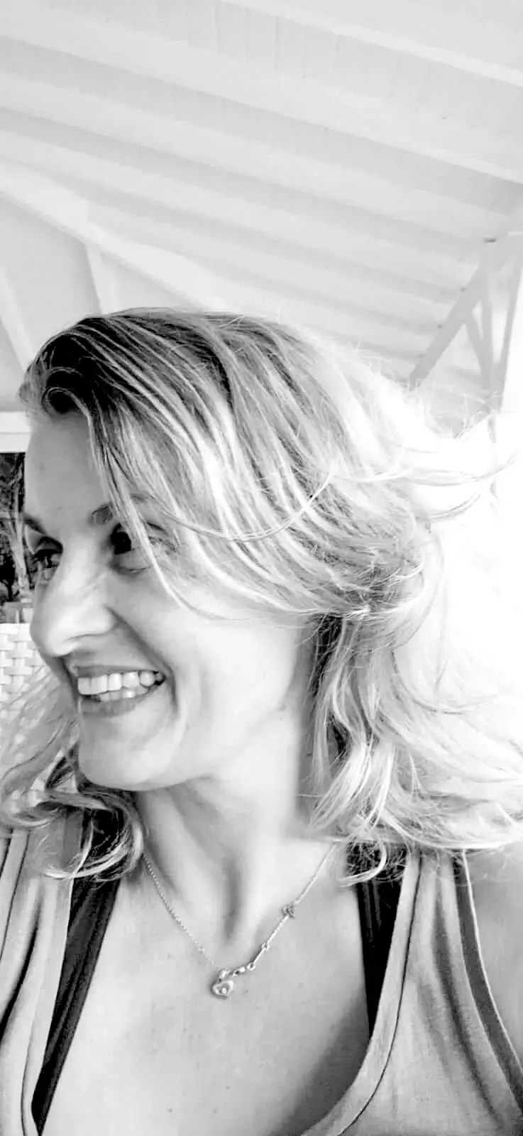 Portrait en noir et blanc d'une femme souriante avec des cheveux bouclés portant un pendentif, dans un endroit lumineux