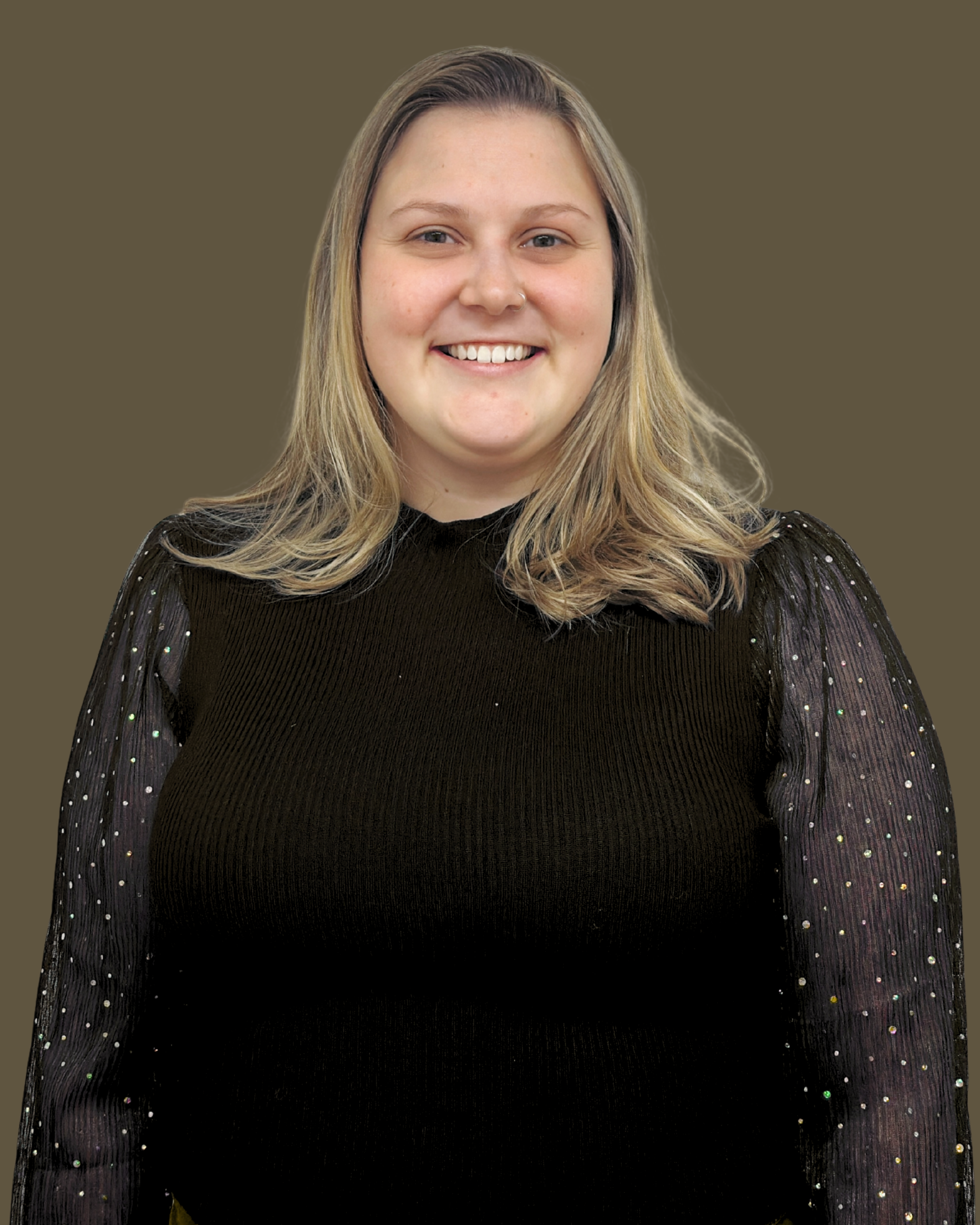A young woman with shoulder-length blonde hair, smiling, wearing a black top with sheer, sparkly sleeves, standing against a plain brown background.