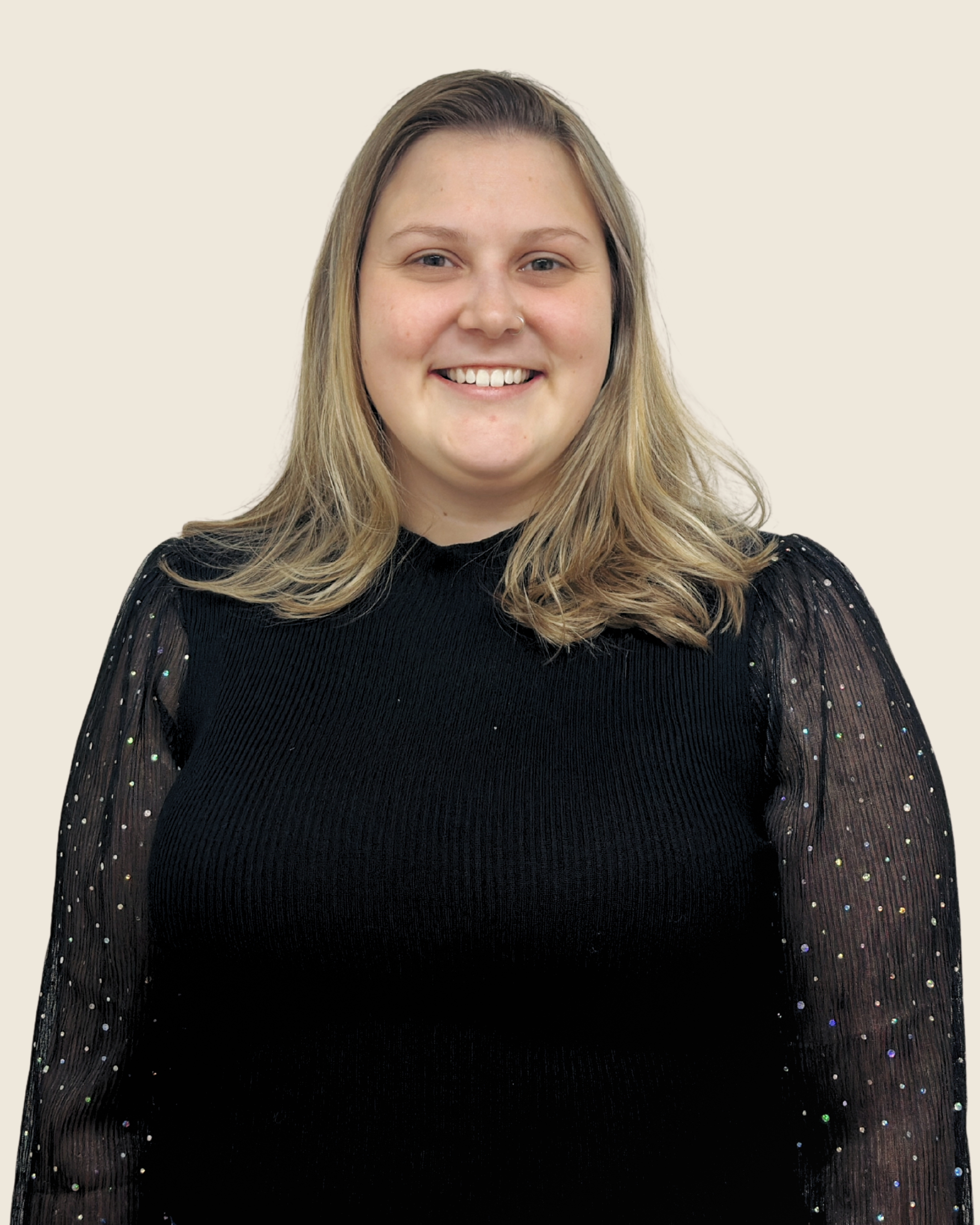 A woman with shoulder-length blonde hair wearing a black top with sheer, sparkly sleeves, smiling at the camera.