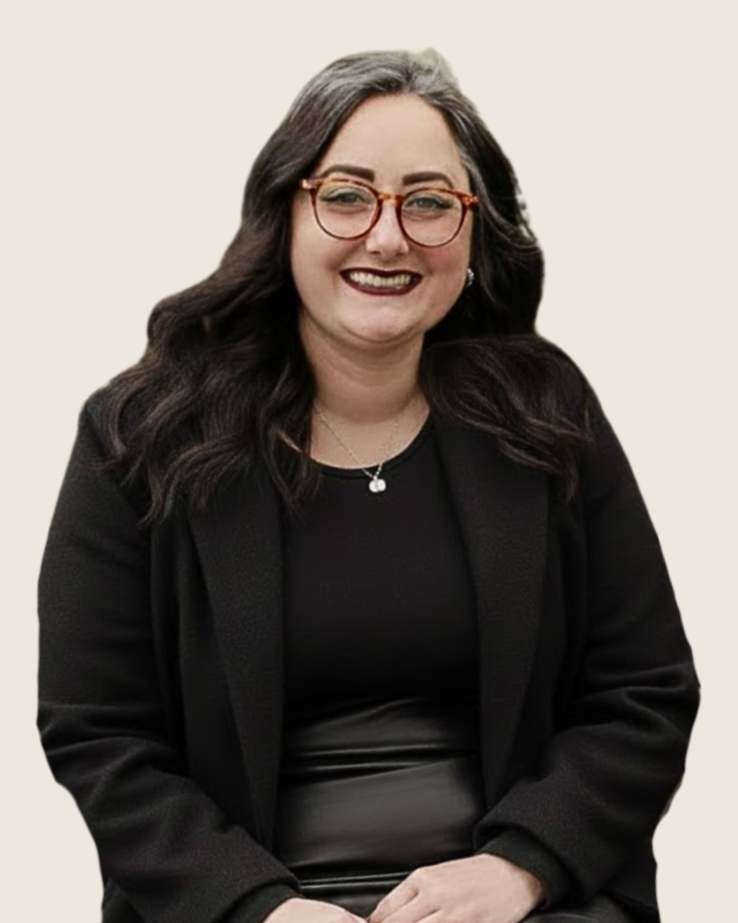 A woman with long dark hair, glasses, and a black blazer sitting and smiling.