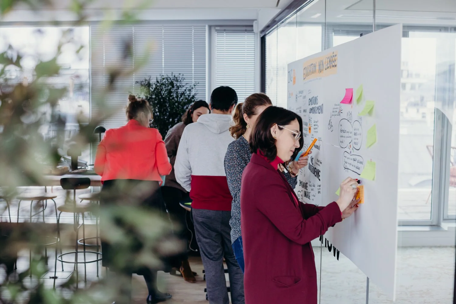 Groupe de personnes collabore autour d'une grande affiche blanche avec des notes autocollantes dans un bureau moderne.