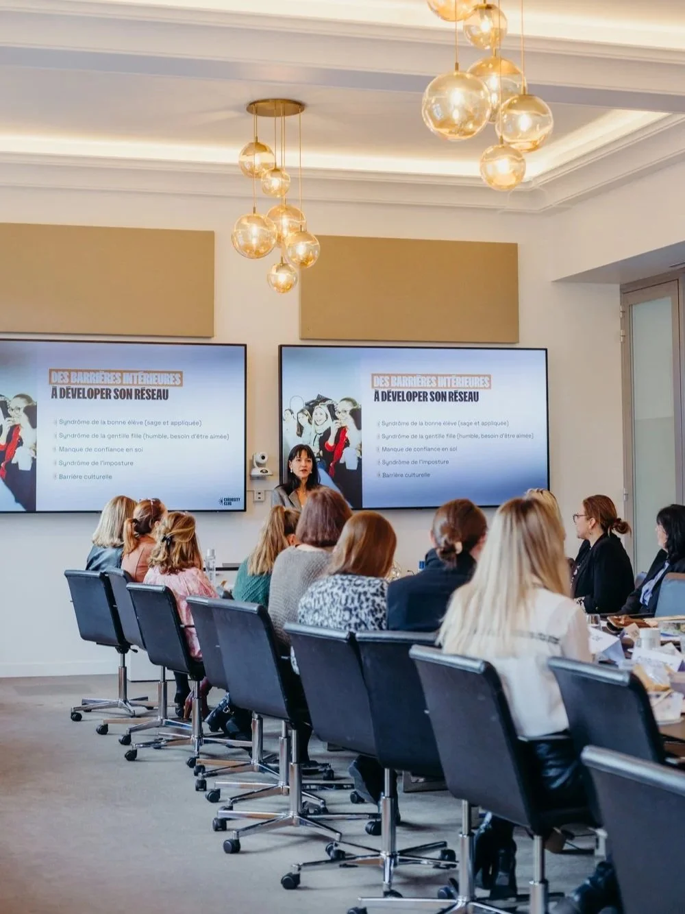 Une salle de conférence avec des personnes assises autour d'une longue table, une femme parlant devant deux grands écrans qui affichent un diaporama sur le développement d'un réseau.