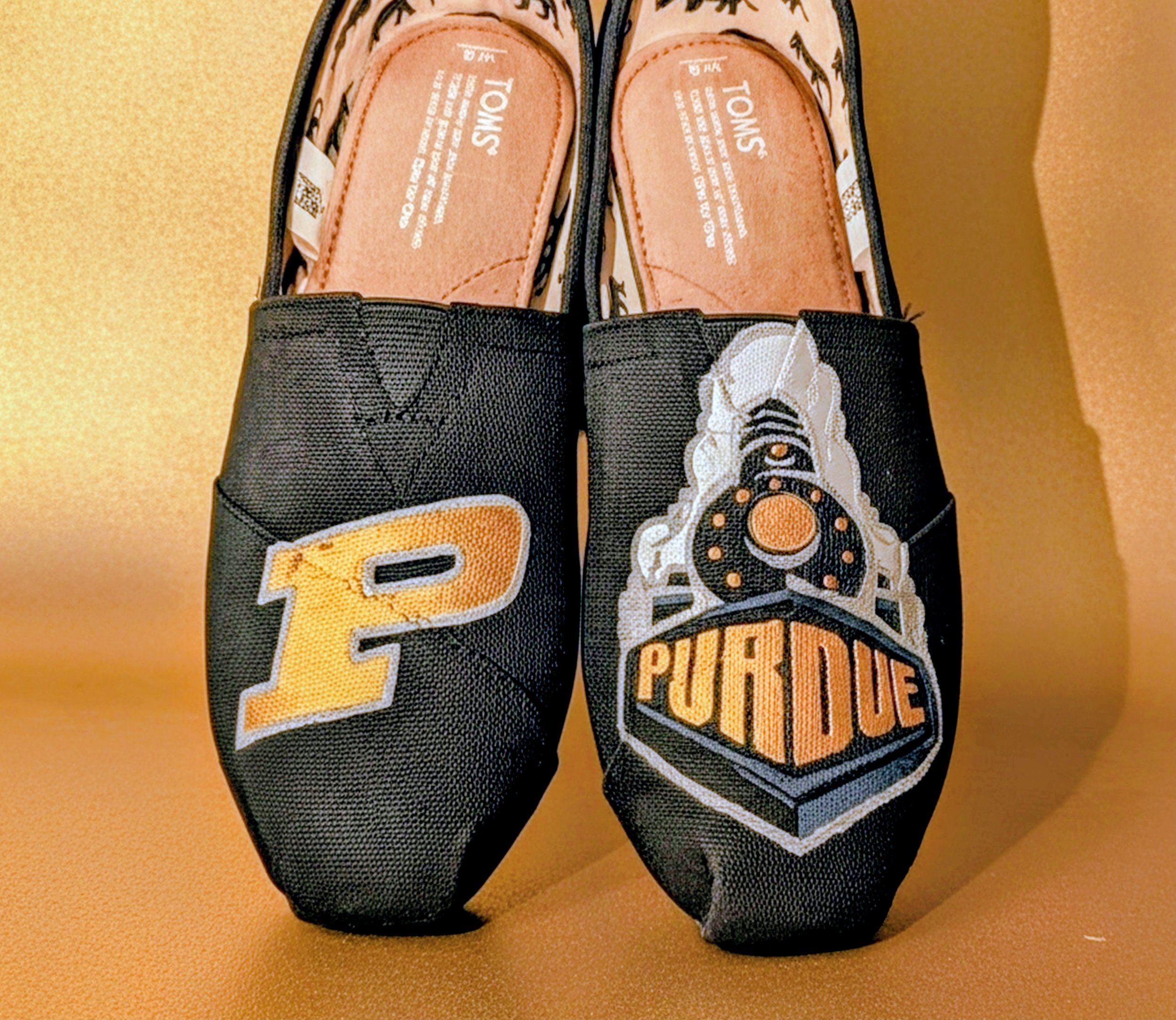 Pair of slip-on shoes with Purdue University logos, one with a yellow letter 'P' and the other with a graphic of a train and the word 'PURDUE' on a black background.