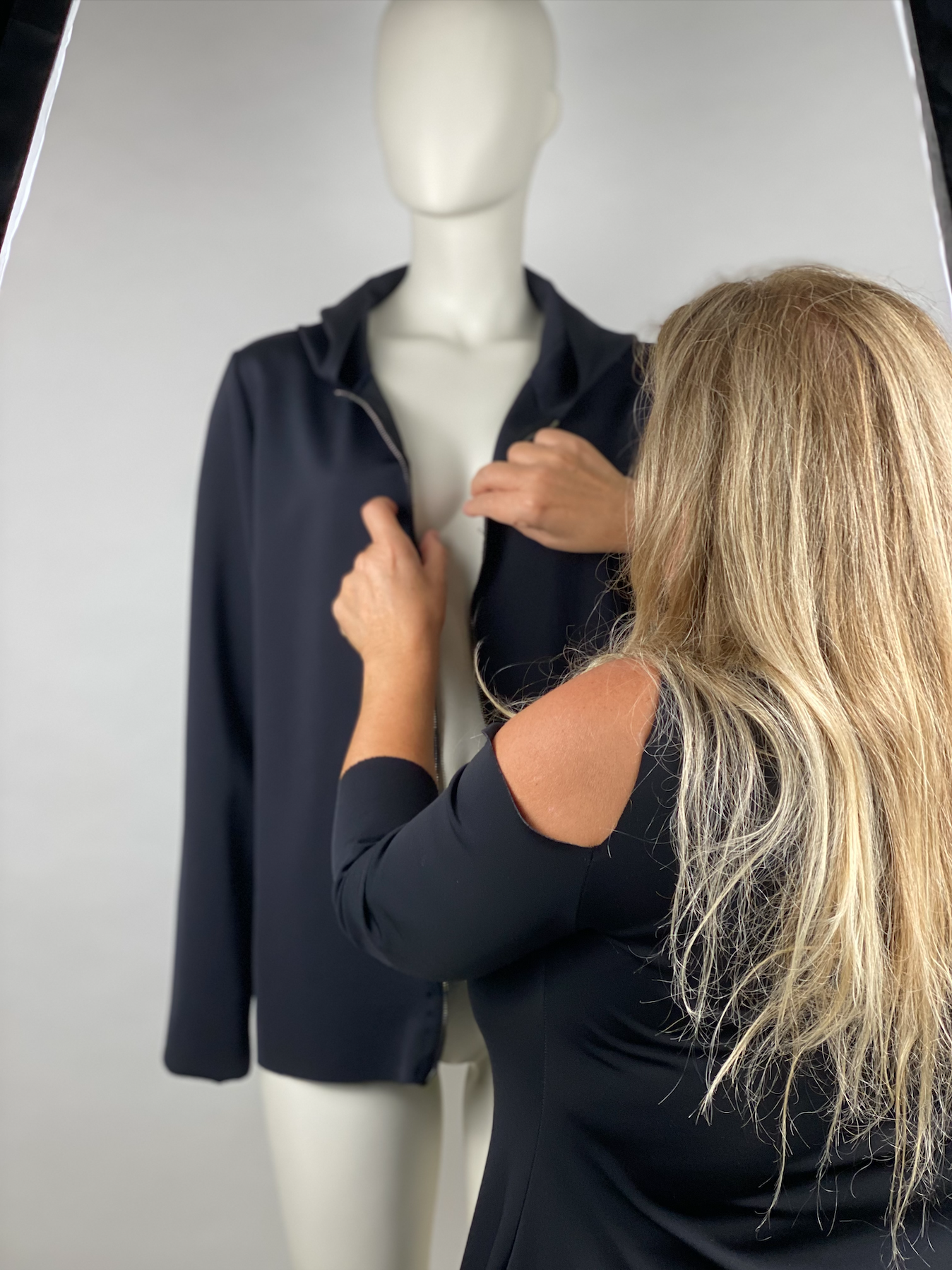 Una donna con i capelli lunghi e biondi sta indossando una giacca nera su un manichino bianco.
