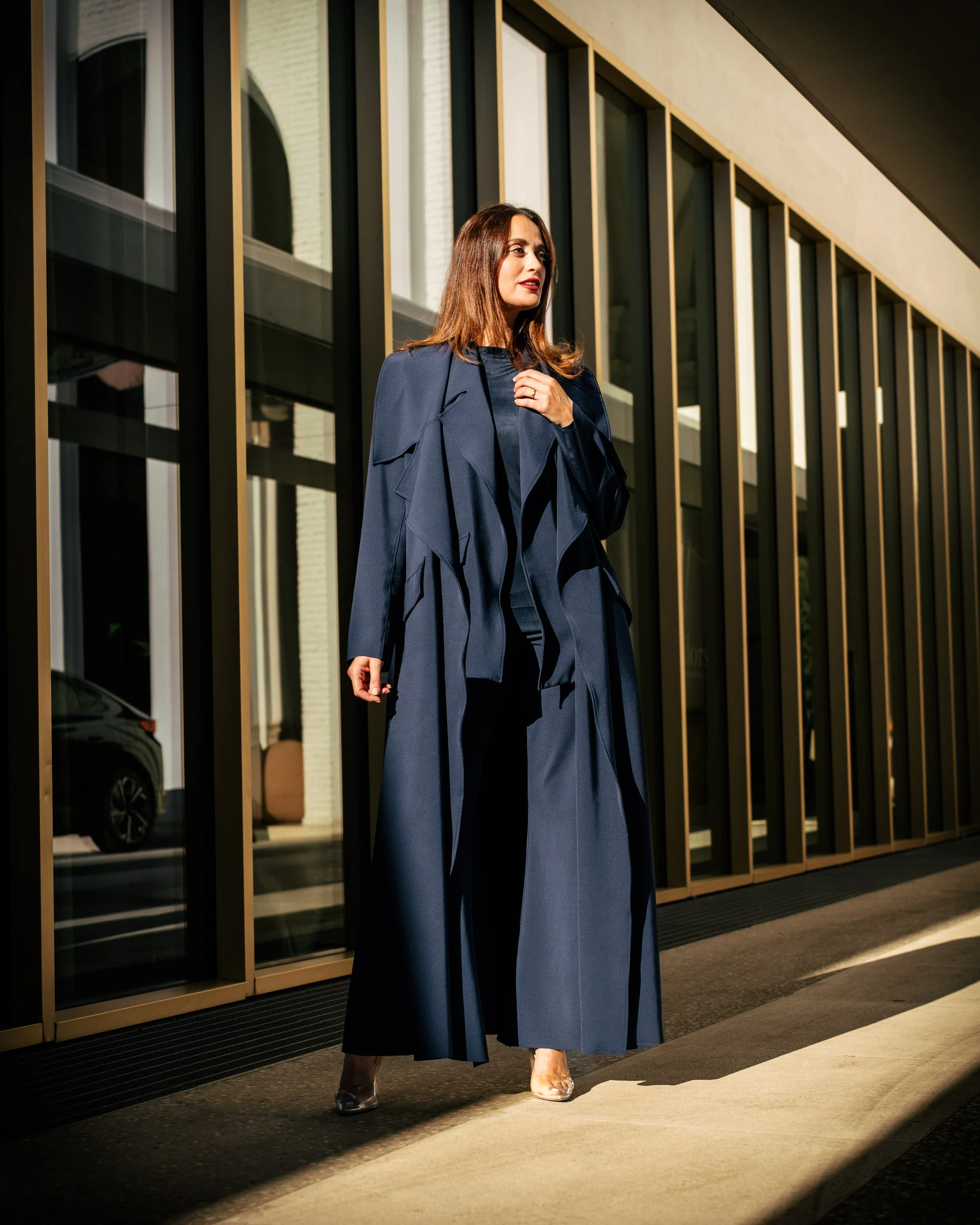 Donna in abiti eleganti blu scuro cammina davanti a un edificio con grandi vetrate e cornici in oro