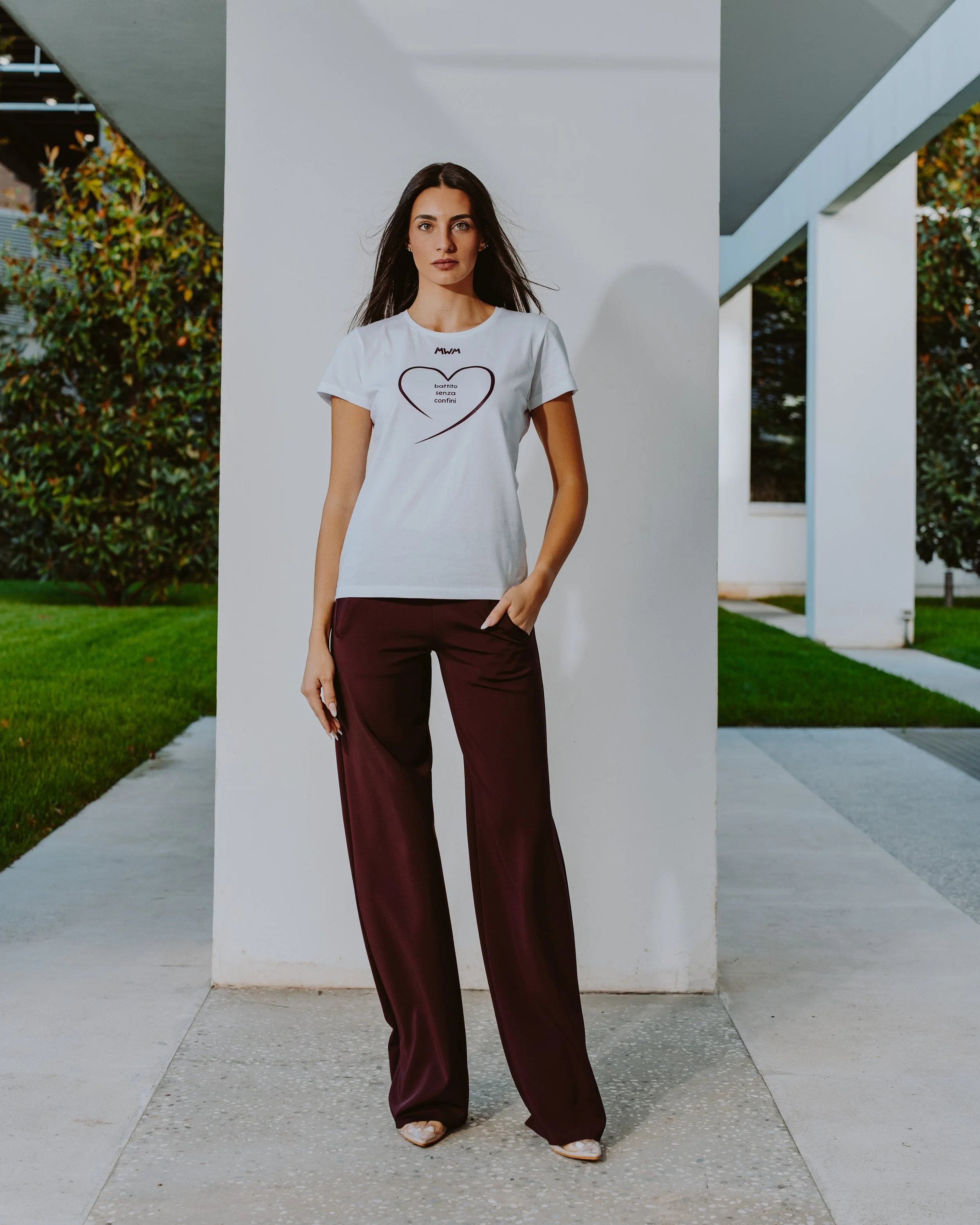 Donna in abiti eleganti in piedi davanti a un edificio moderno con verde sullo sfondo.