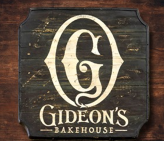 A wooden sign with a white letter 'G' and the words 'Gideon's Bakehouse' on a dark background.