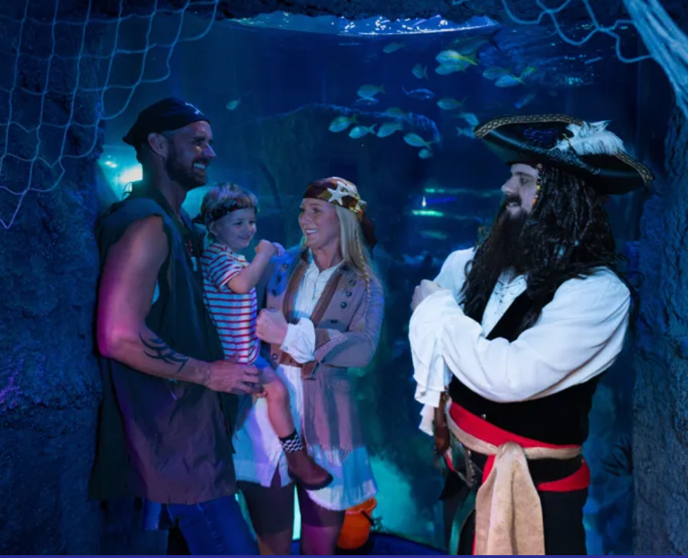 A family dressed as pirates at an aquarium with sea creatures in the background.