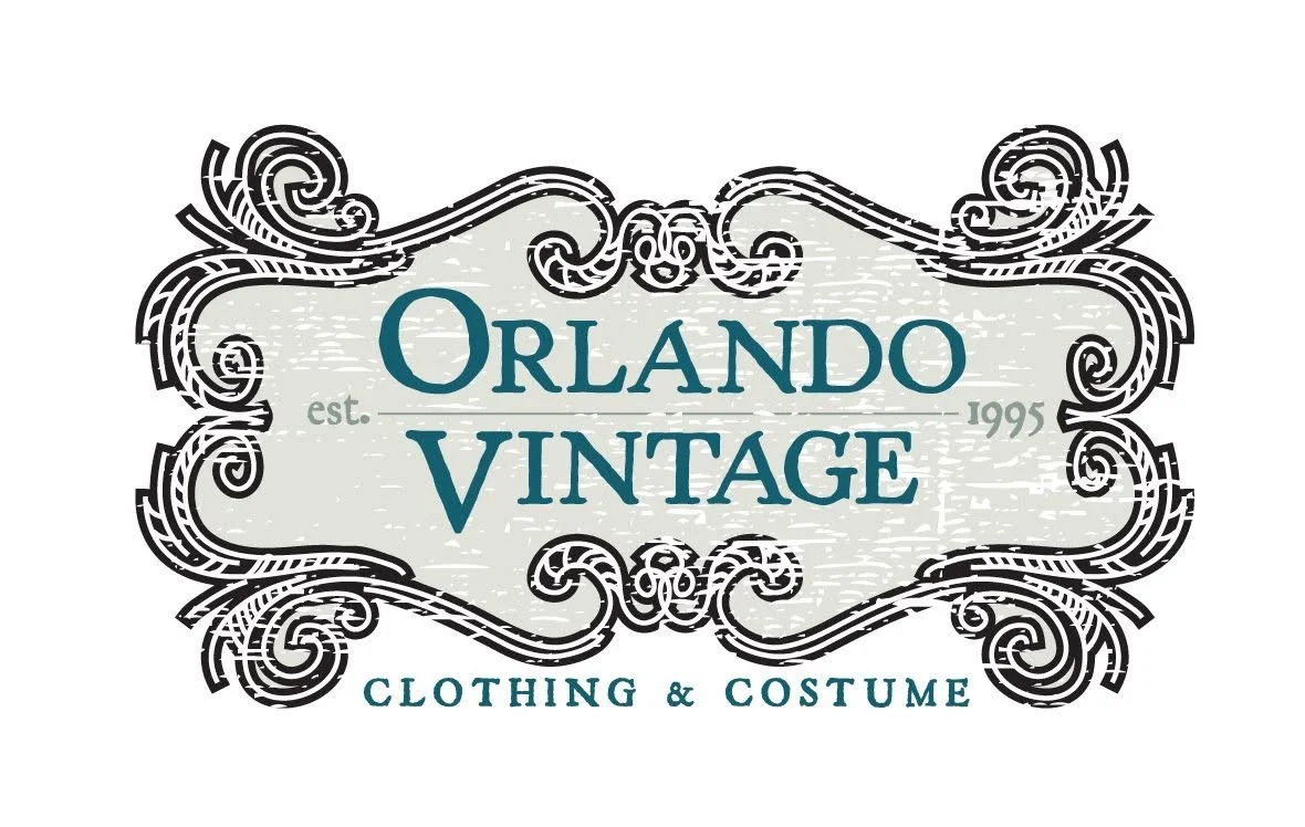 Vintage clothing and costume shop logo with ornate black frame, teal and grey text, and the establishment year 1995.