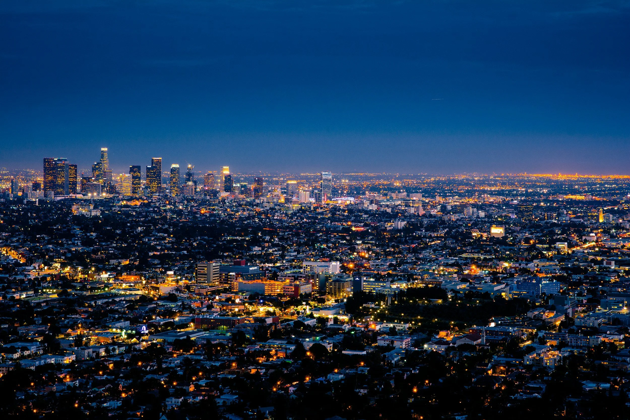 Nighttime city skyline of Los Angeles with illuminated skyscrapers and residential areas.