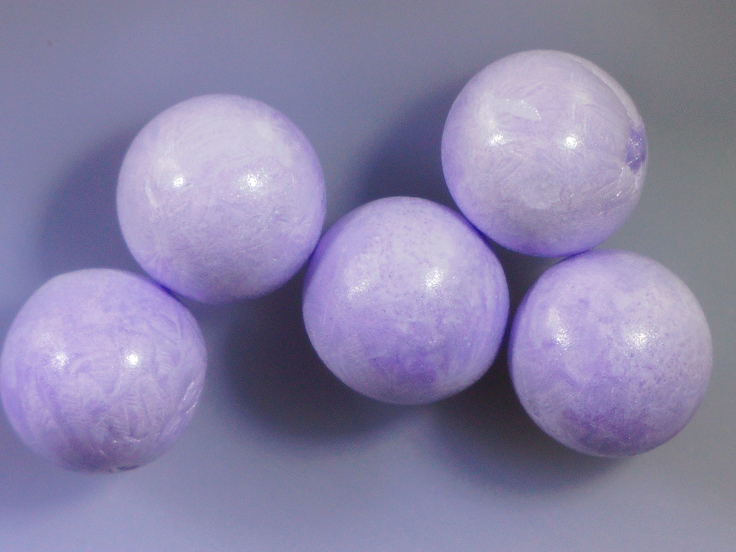 Close-up of several purple Lyobeads arranged on a dark surface.
