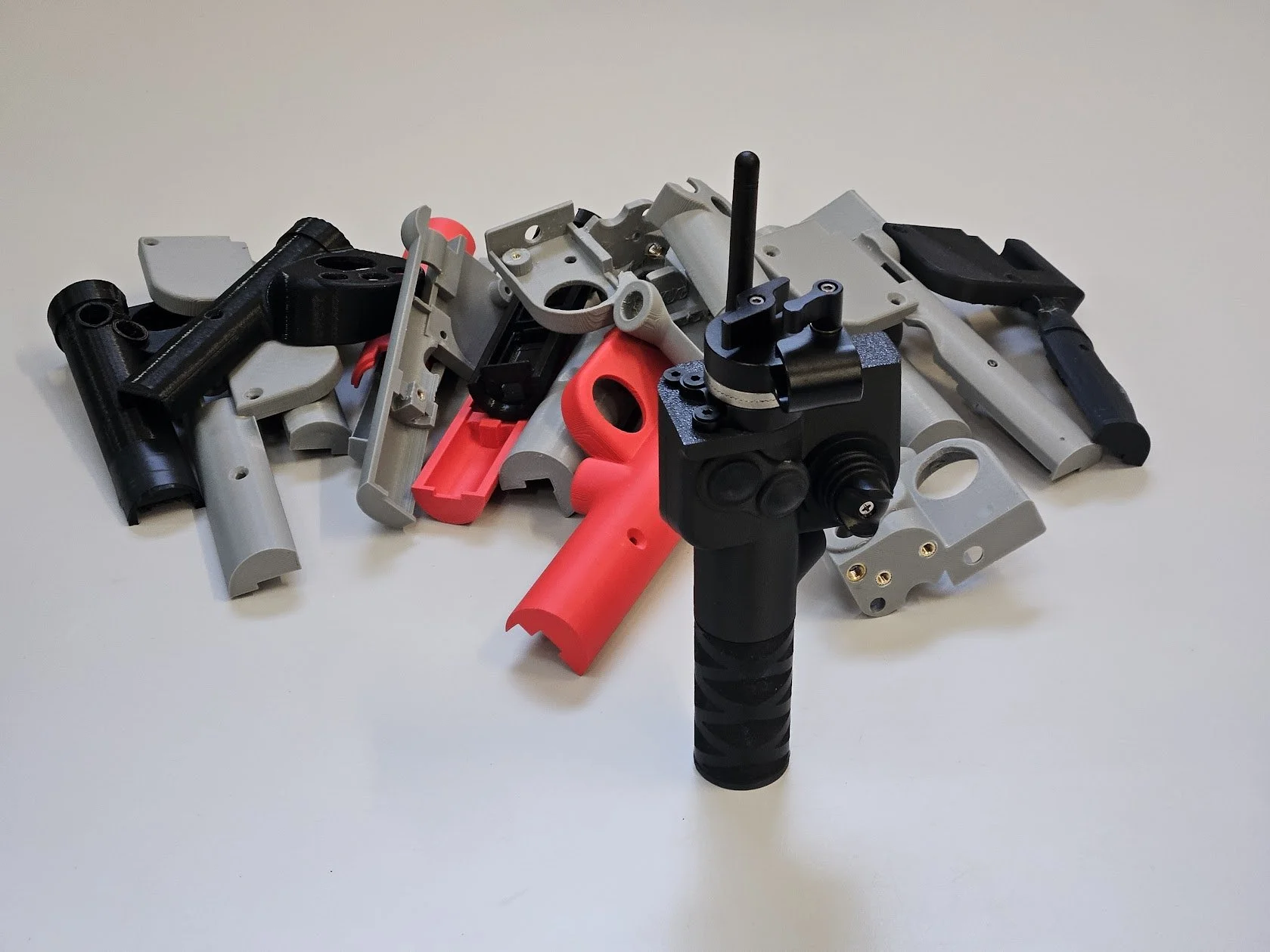 Prototype de pistolet futuriste en plastique noir avec manche en caoutchouc, entouré de plusieurs pièces de plastique gris, noir et rouge.