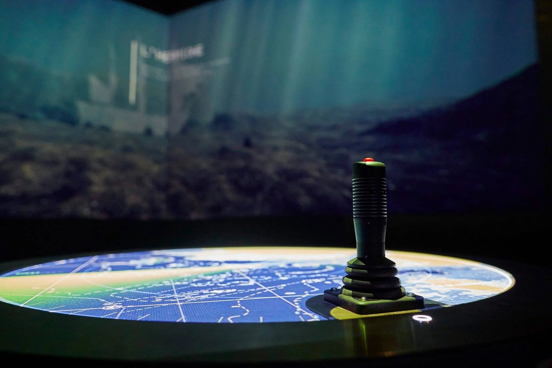 Un joystick placé sur une table ronde avec un écran de projection en arrière-plan.