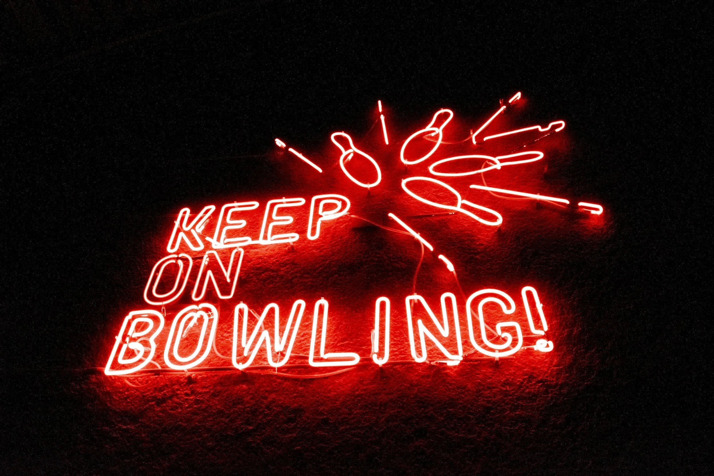 Red neon sign reading 'Keep On Bowling!' with a bowling ball and pin illustration, on a dark background.