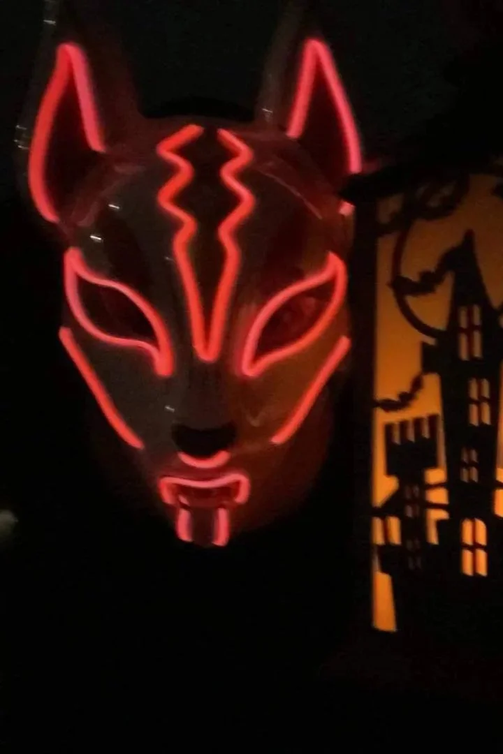 Masque lumineux de renard avec des lignes rouges néon, dans un environnement sombre avec une décoration de maison hantée en arrière-plan.