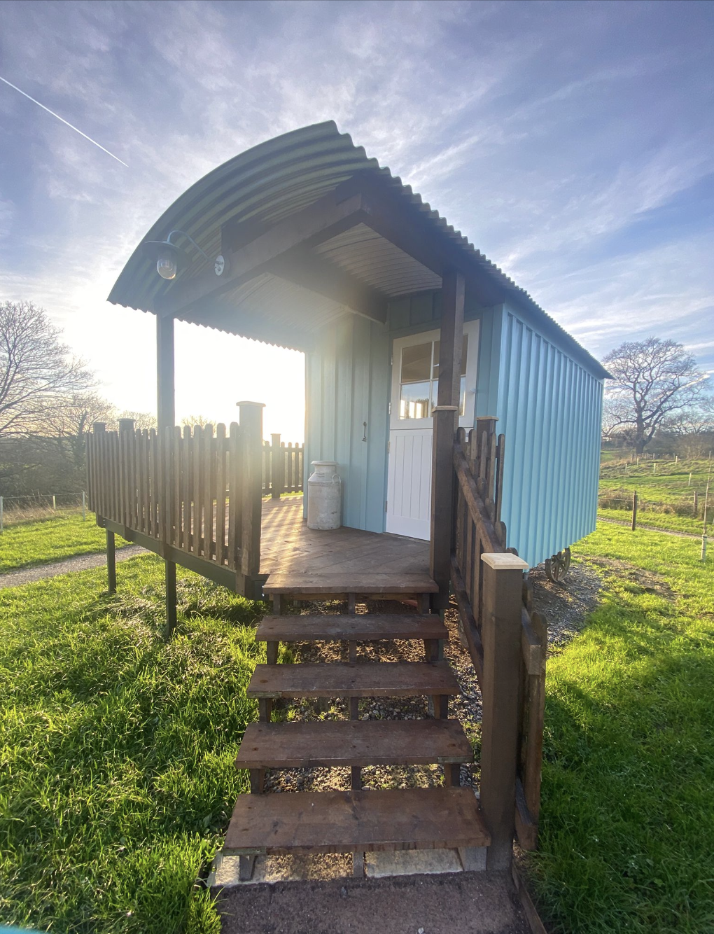 View of the shepherds hut from the front. The sun is shining, the sky is blue and there is beautiful light shining through the shepherds hut 