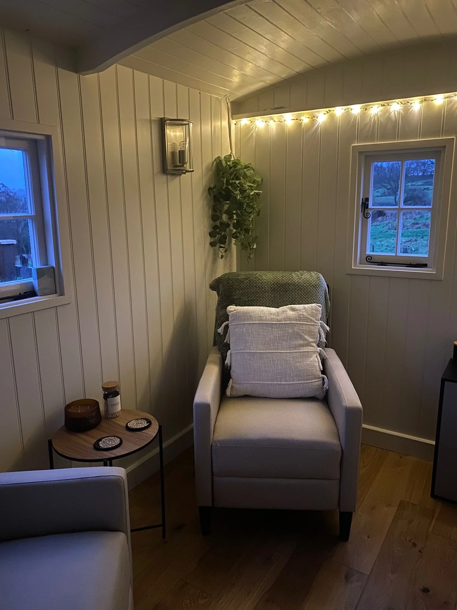 Inside of the shepherds hut are 2 comfy looking armchairs. there's fairy lights and soft furnishings. The space looks very inviting and warm. 