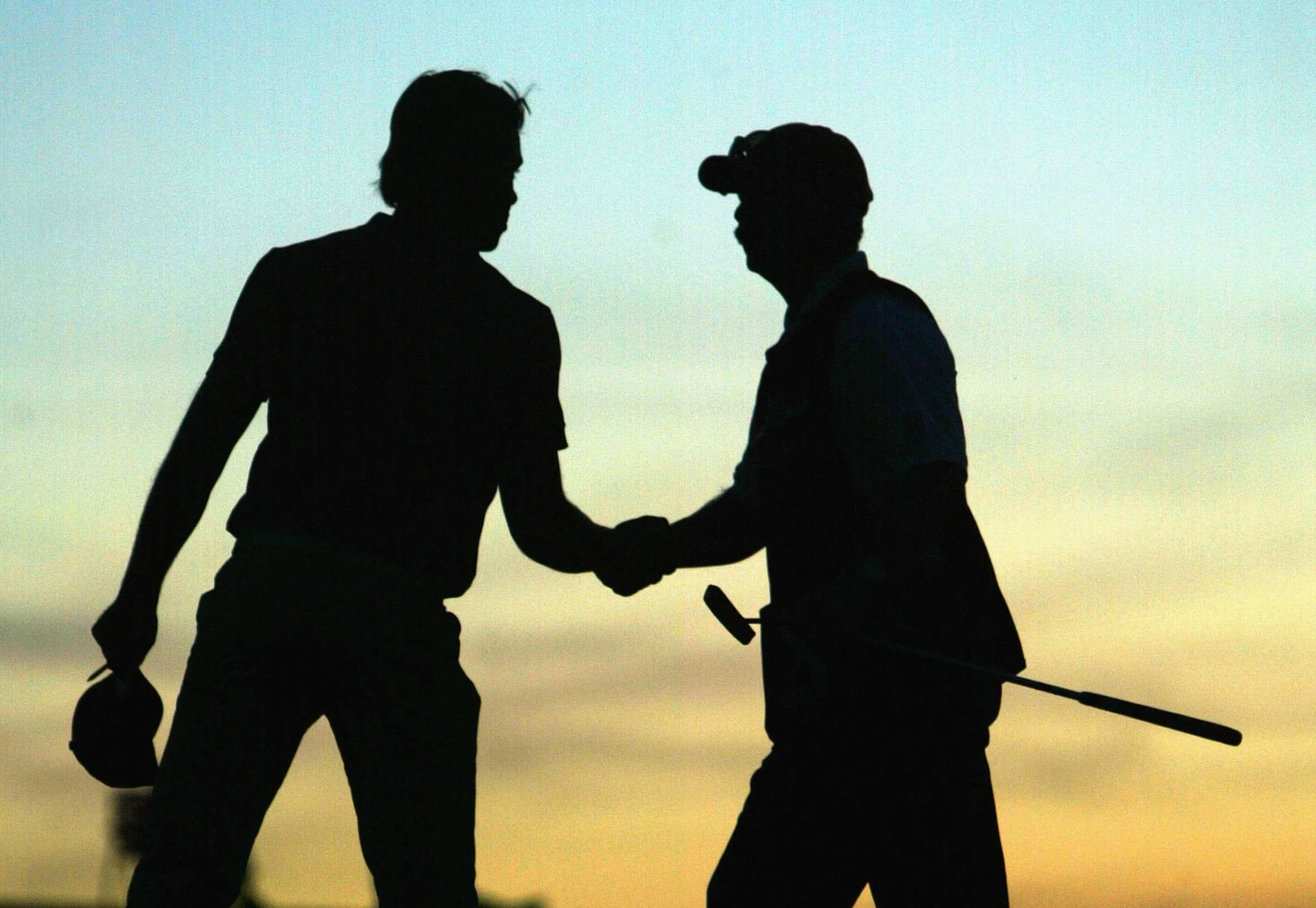 Silhouettes of two men shaking hands, one wearing sunglasses and holding a tool, against a sunset sky.