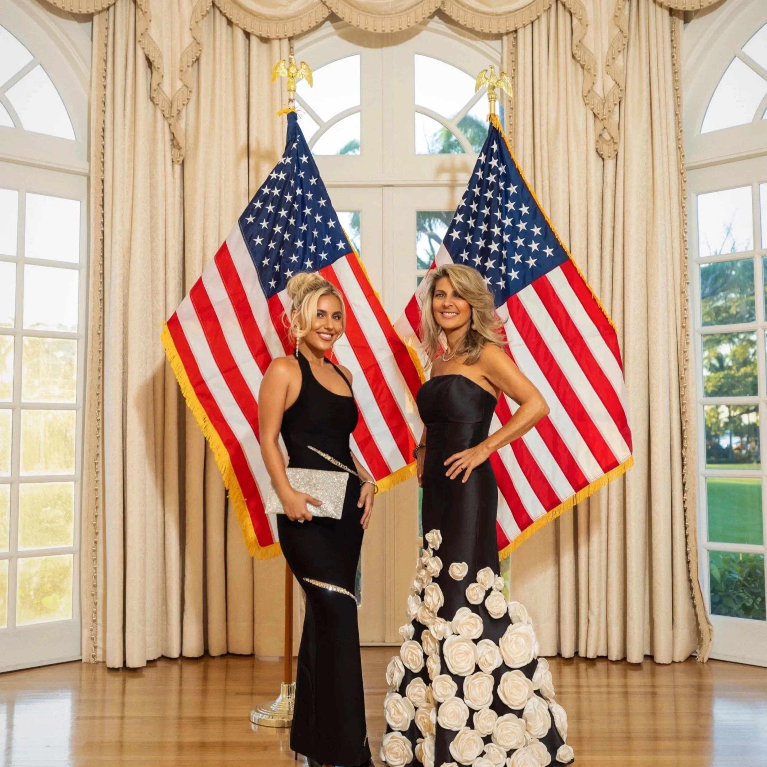 Two women in black gowns standing in front of 2 flags at Mar-A-Lago