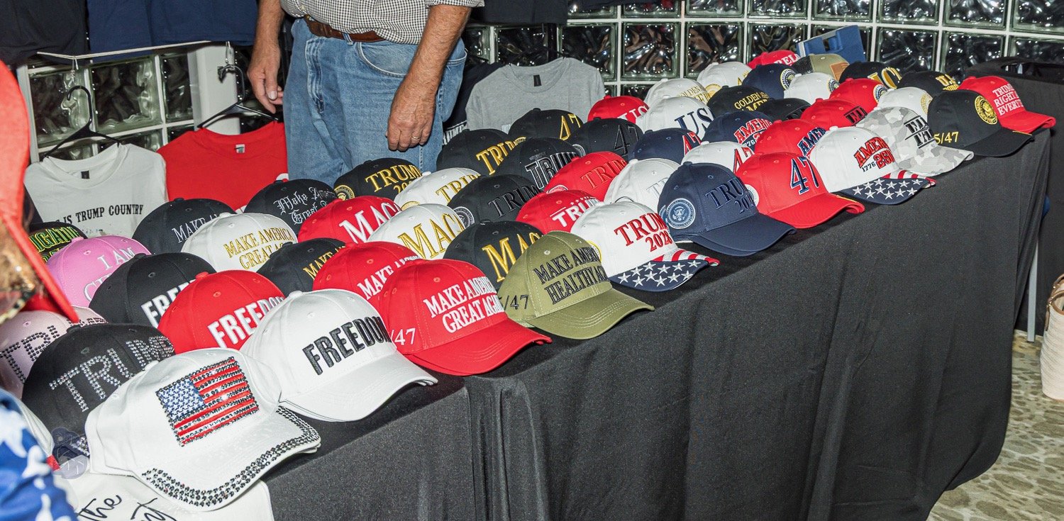 A table displaying various hats and shirts with political slogans including 'FREEDOM,' 'MAKE AMERICA GREAT AGAIN,' and 'TRUMP 2024,' along with patriotic designs and campaign messages.