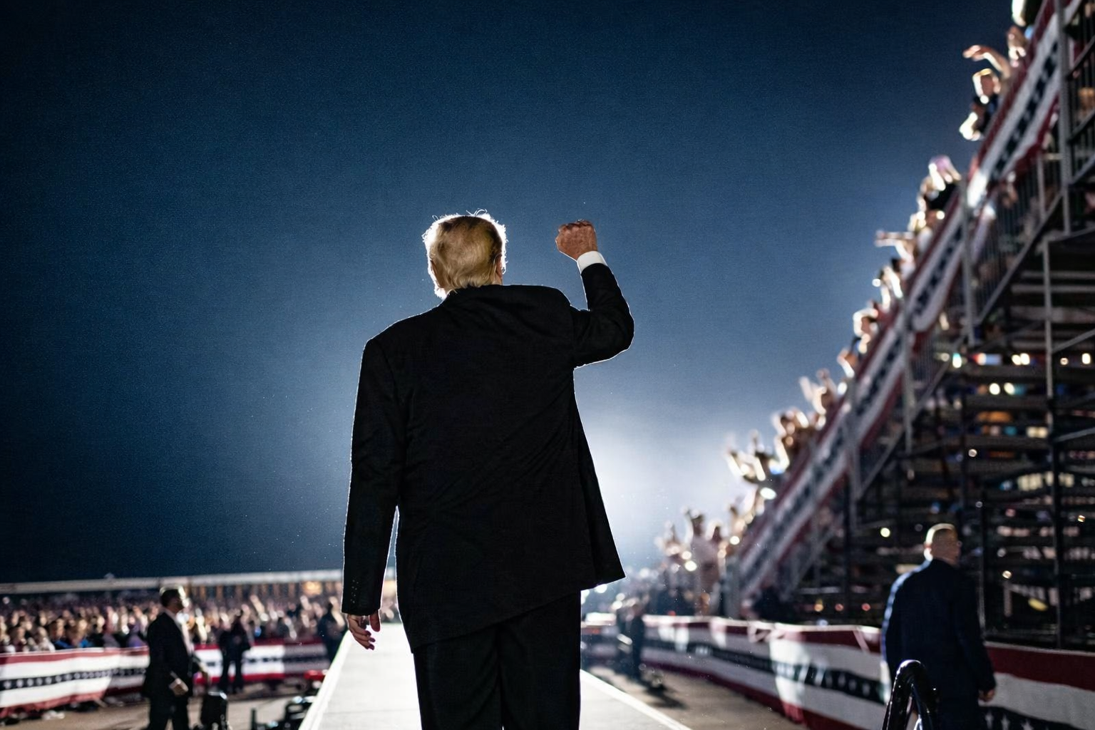 Presidential rally with back of man facing towards crowd holding up fist in the air