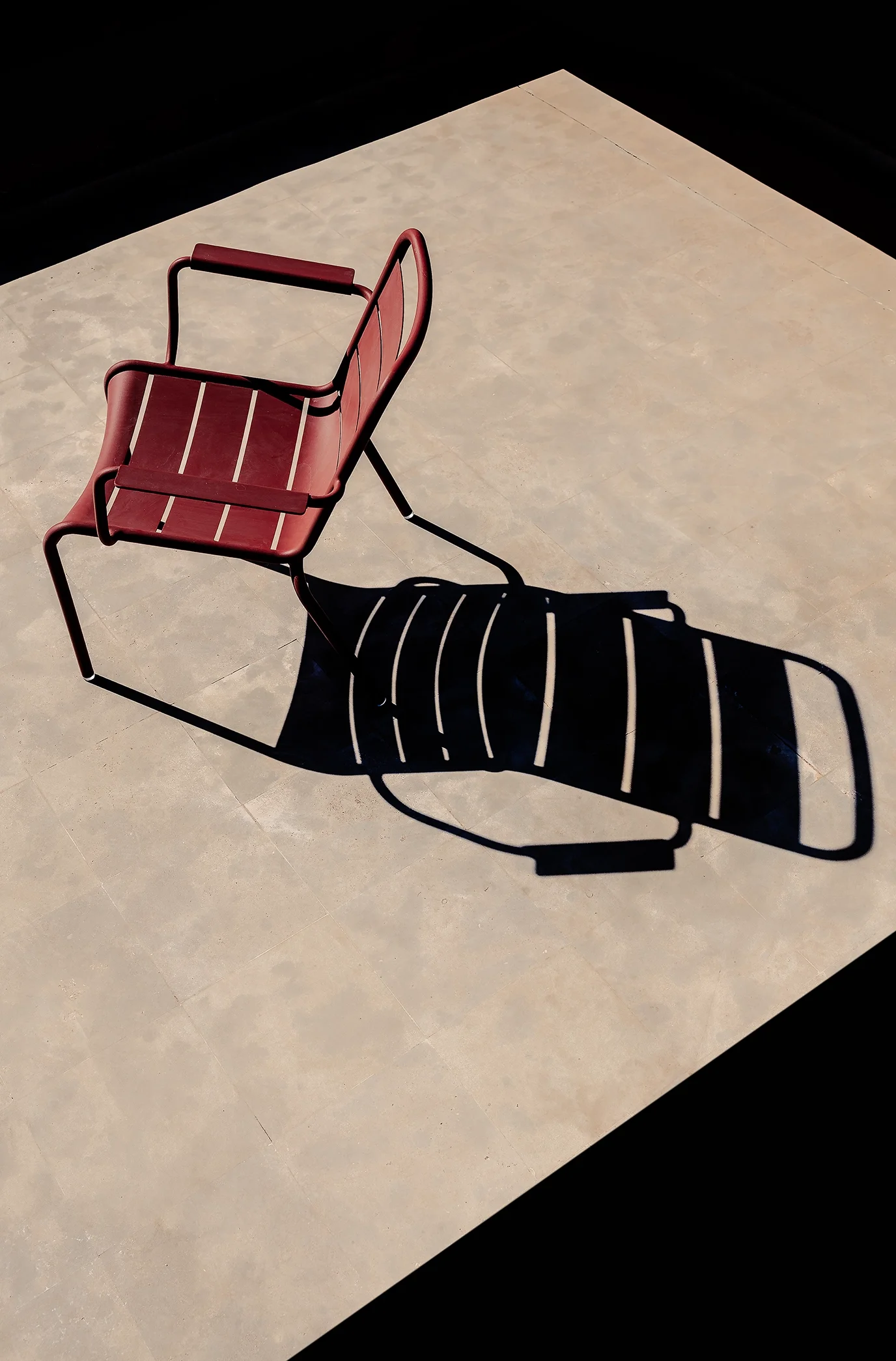 Une chaise rouge avec un cadre en métal, projetant une ombre graphique sur le sol beige