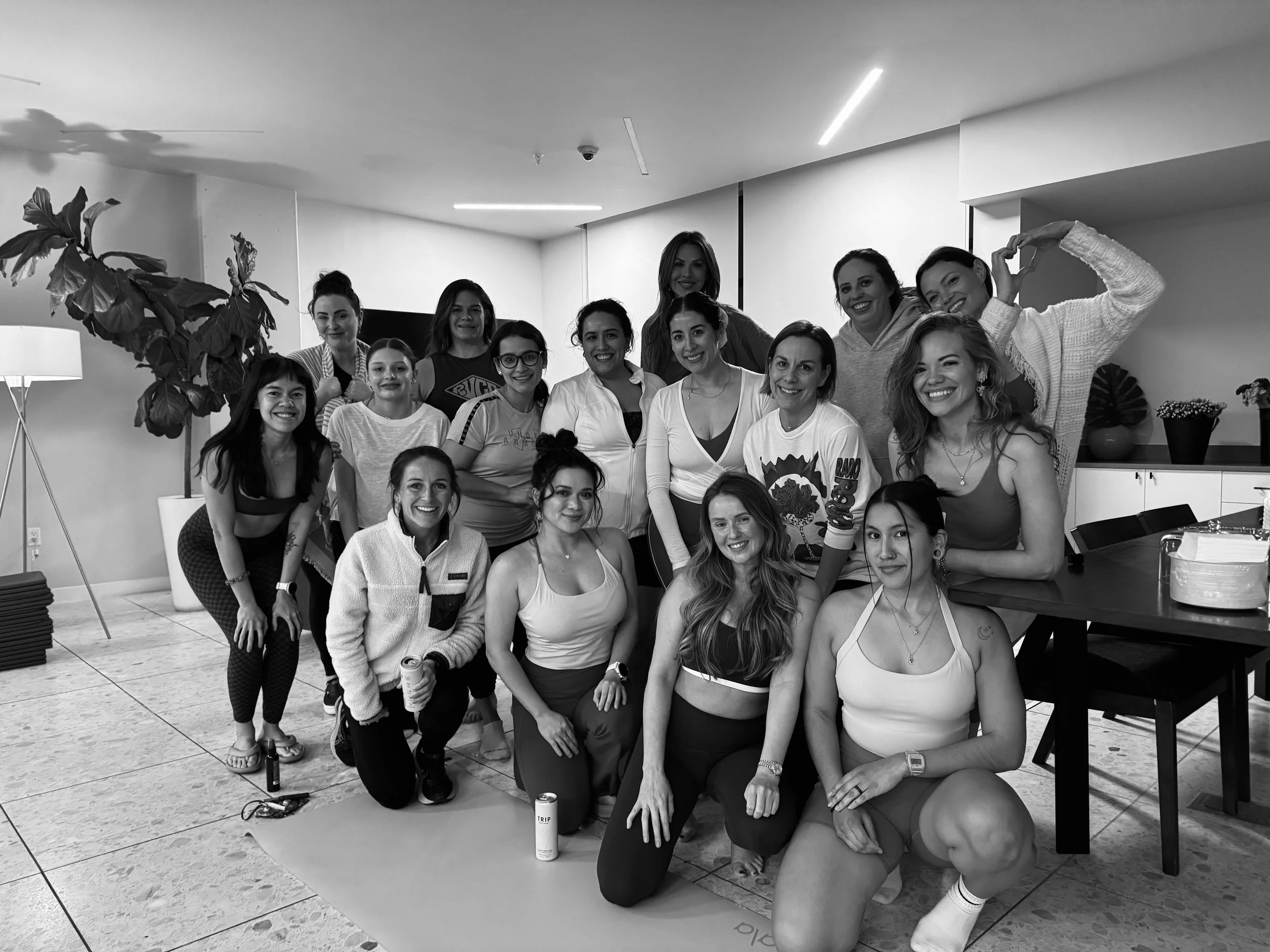 A diverse group of women posing together indoors, smiling, with some making heart gestures with their hands.