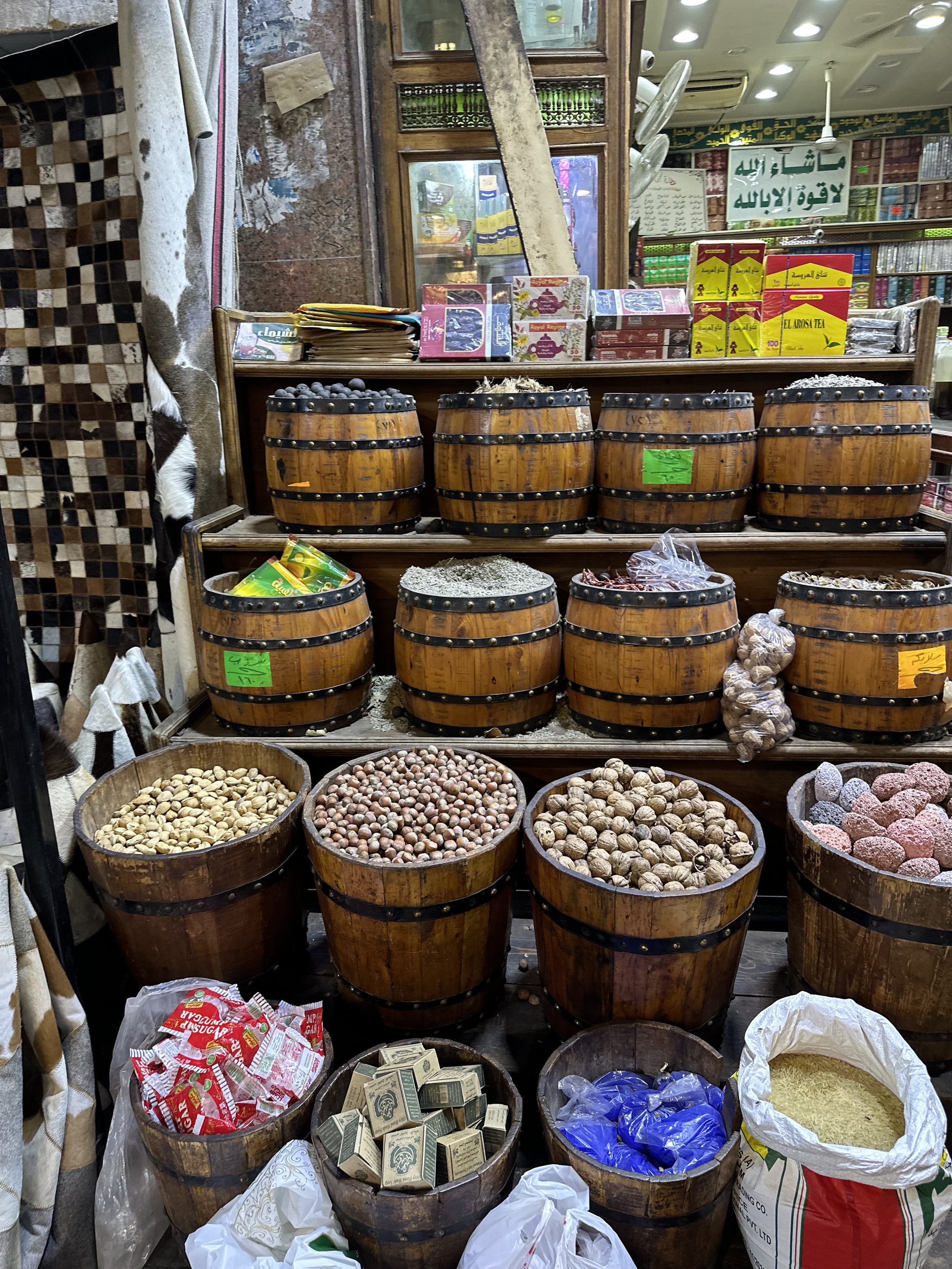 Traditional market stall with wooden barrels filled with different dried fruits and nuts, and packaged goods displayed on shelves in the background.