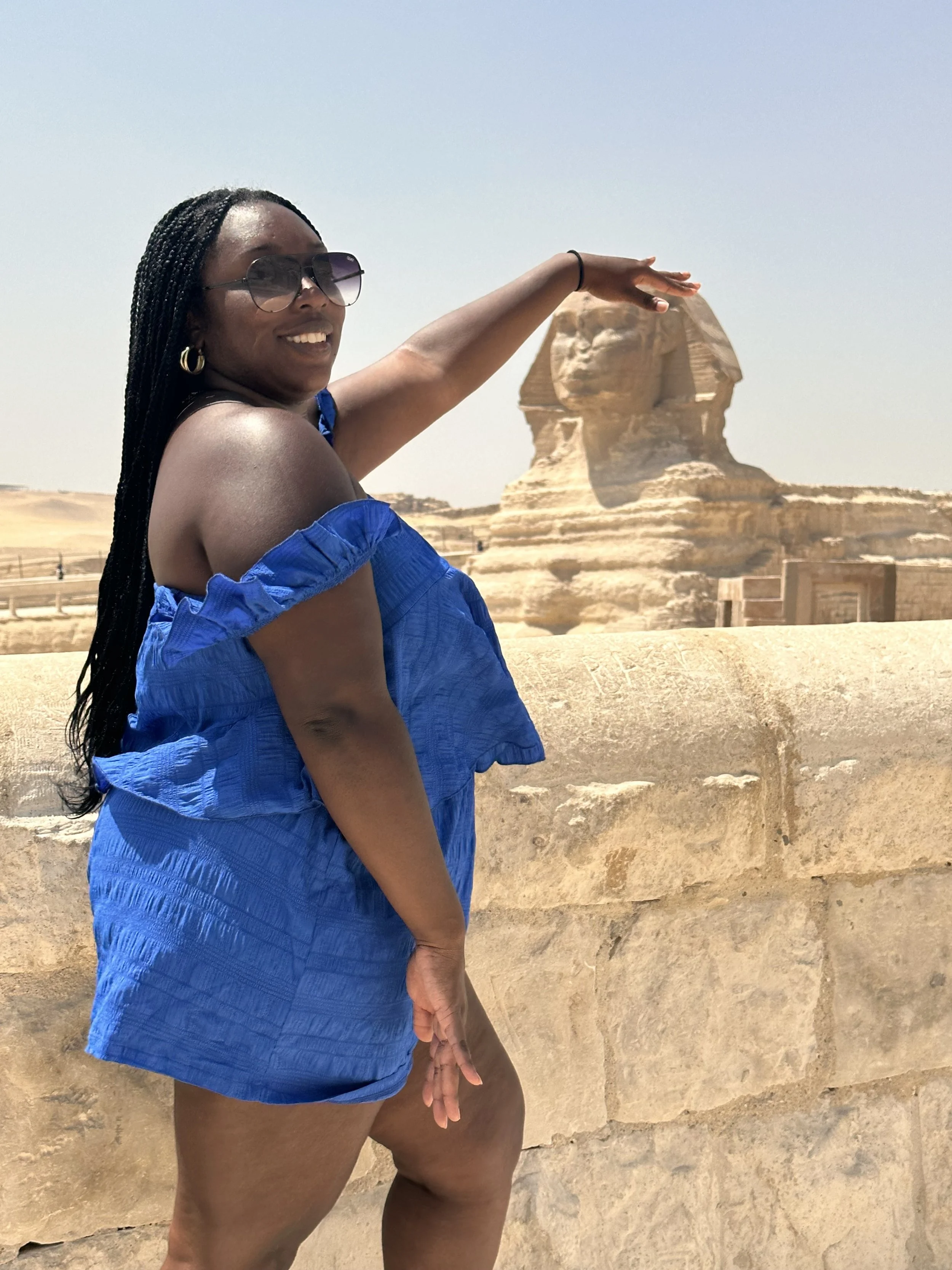 Latrice in a blue off-shoulder dress posing in front of the Sphinx and pyramids in Egypt.