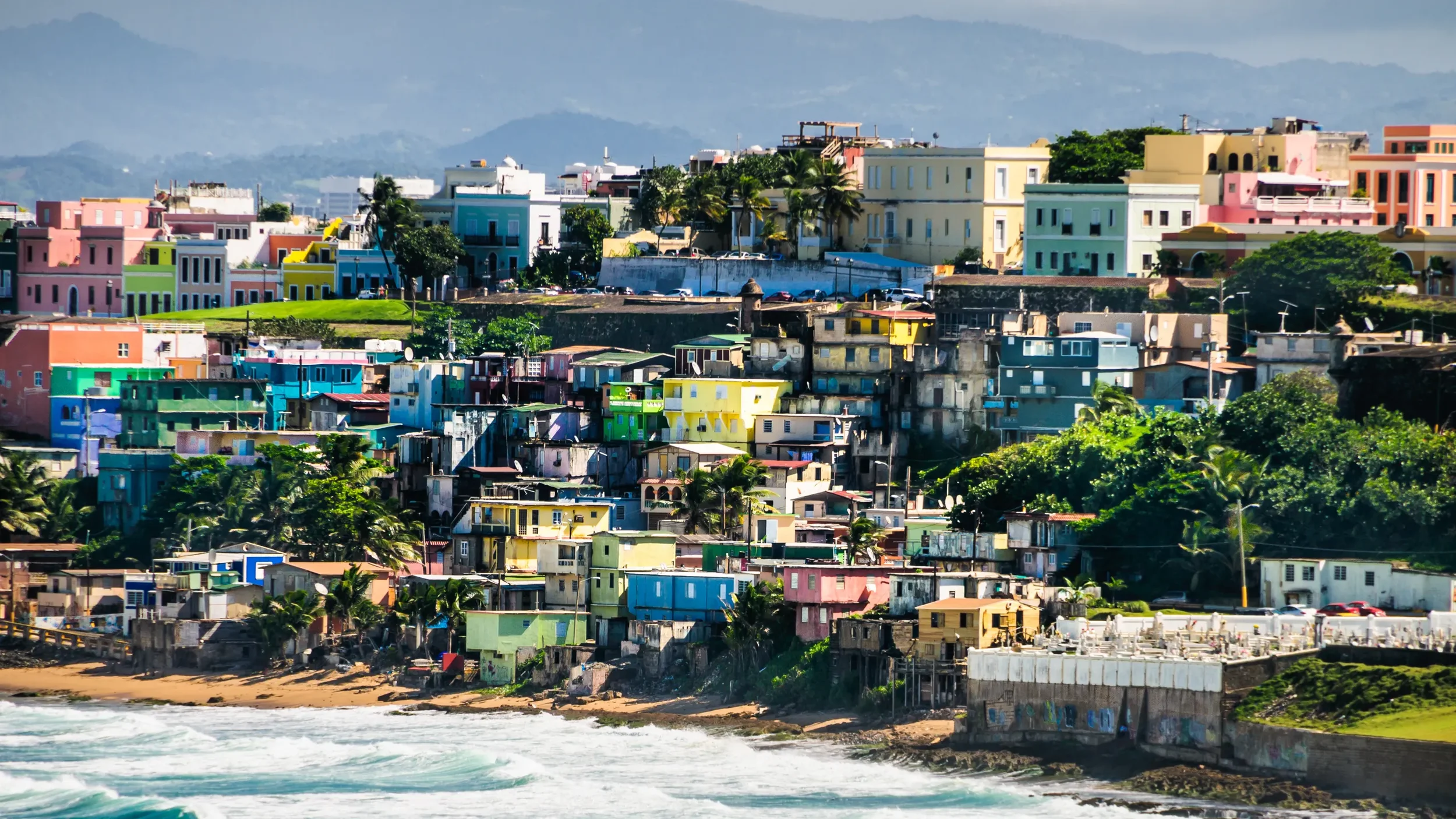 Colorful houses and buildings on a hillside overlooking the ocean with waves crashing on the shore.