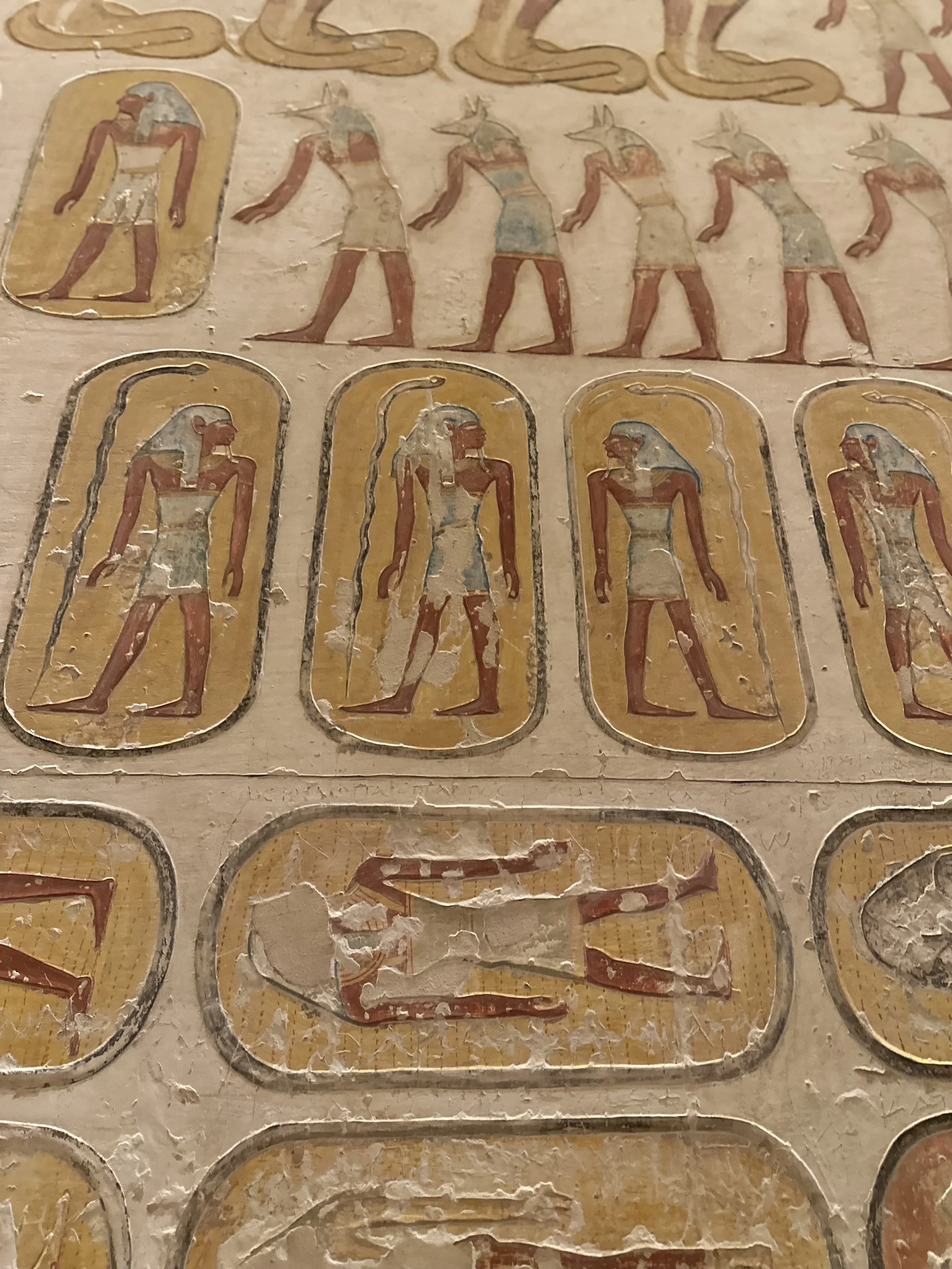 Ancient Egyptian hieroglyphic depicting gods or mythological figures with animal and human features, arranged in rows and columns, with some worn or damaged.