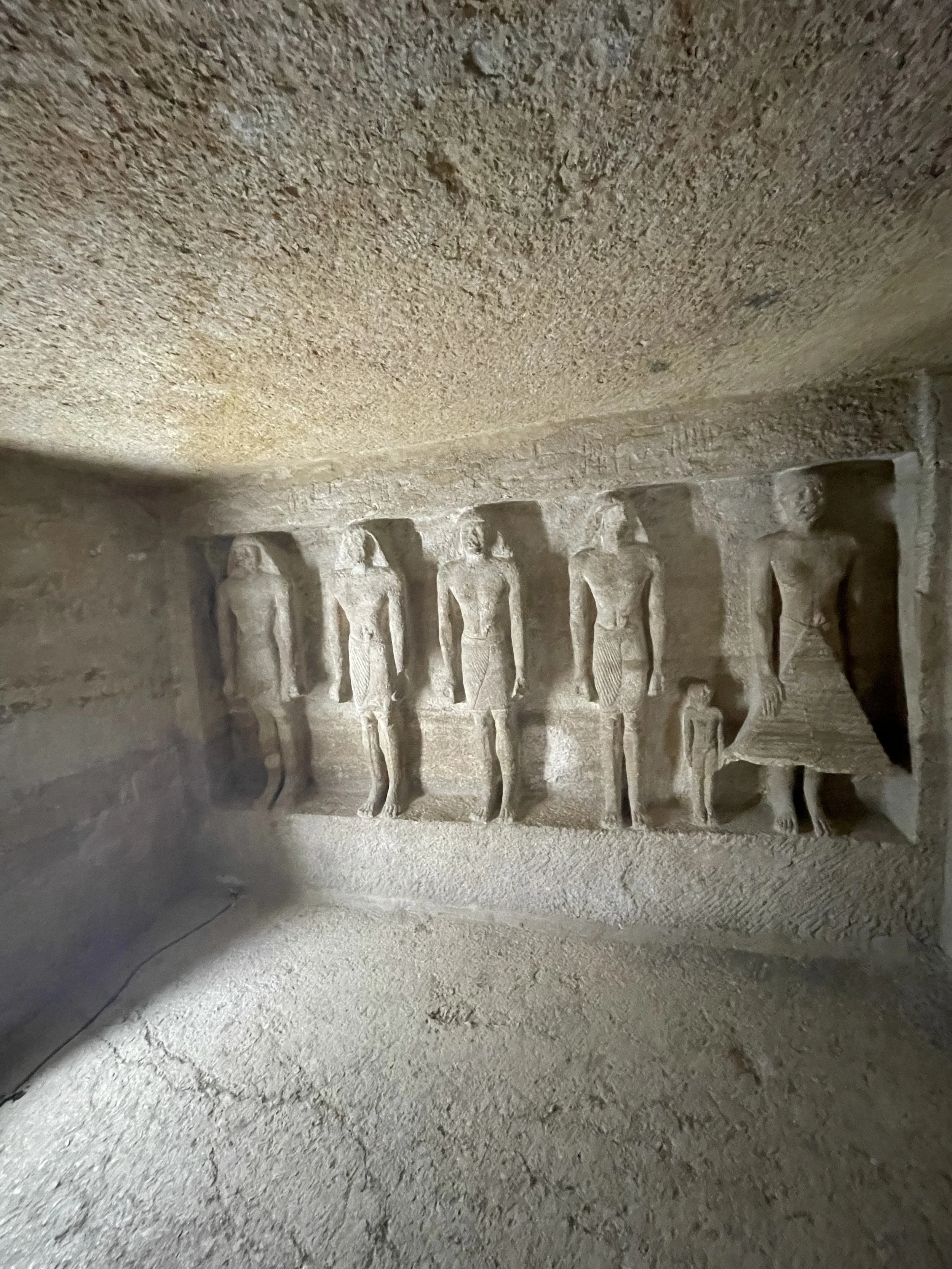 Ancient Egyptian stone relief depicting a row of standing figures, with hieroglyphic inscriptions above them.