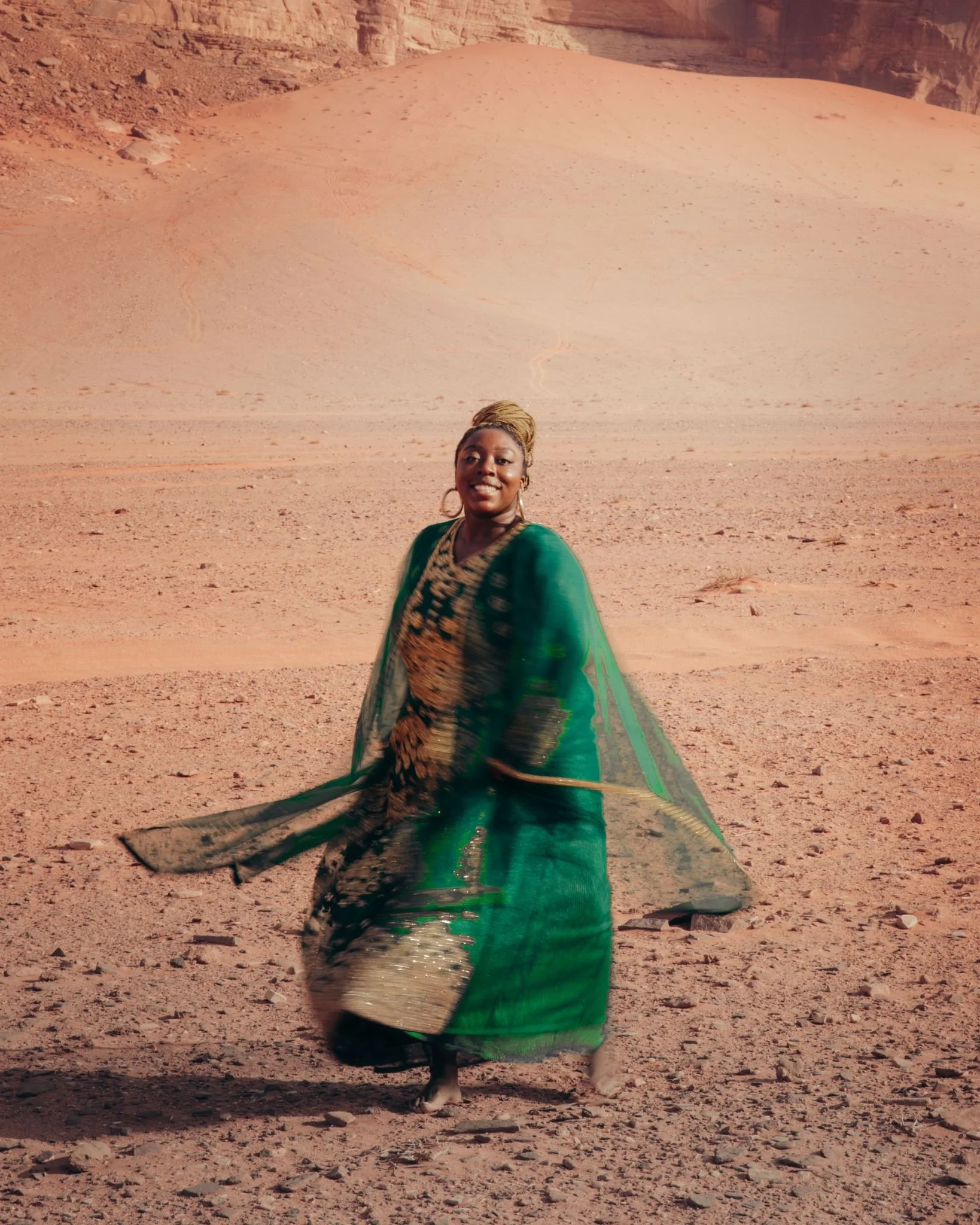 A woman in a colorful dress standing in a desert landscape with sand dunes.
