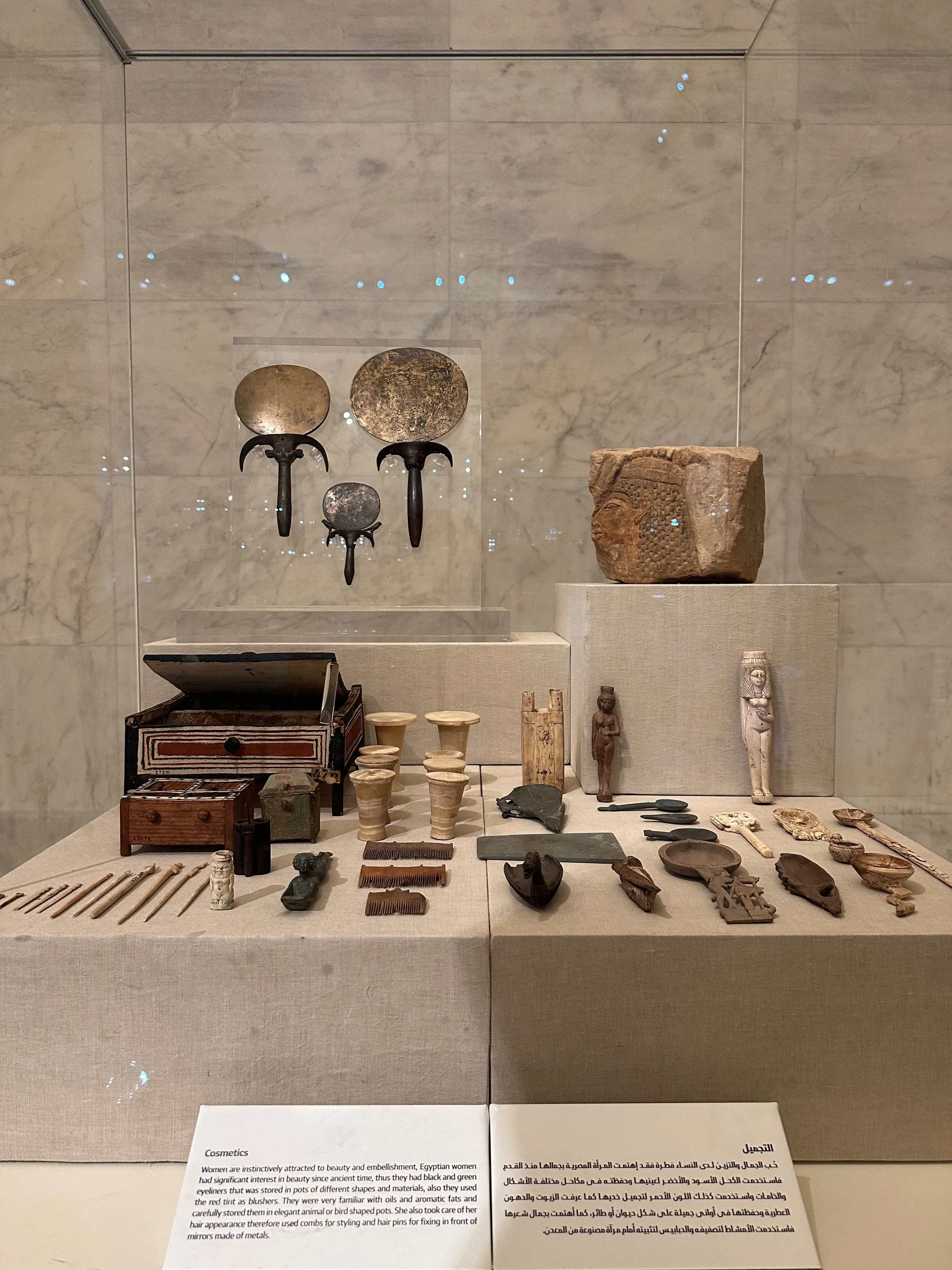 Ancient Egyptian artifacts displayed in a museum exhibit, including clay tablets, small statues, jewelry, and household items.