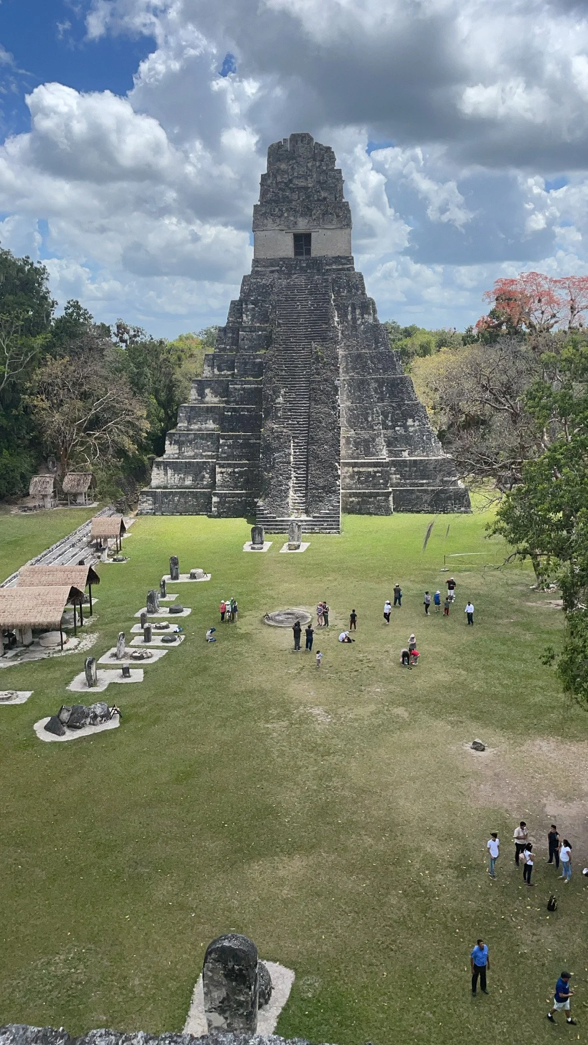 Ancient Mayan pyramid at Tikal ruins in Guatemala with visitors walking around and a partly cloudy sky