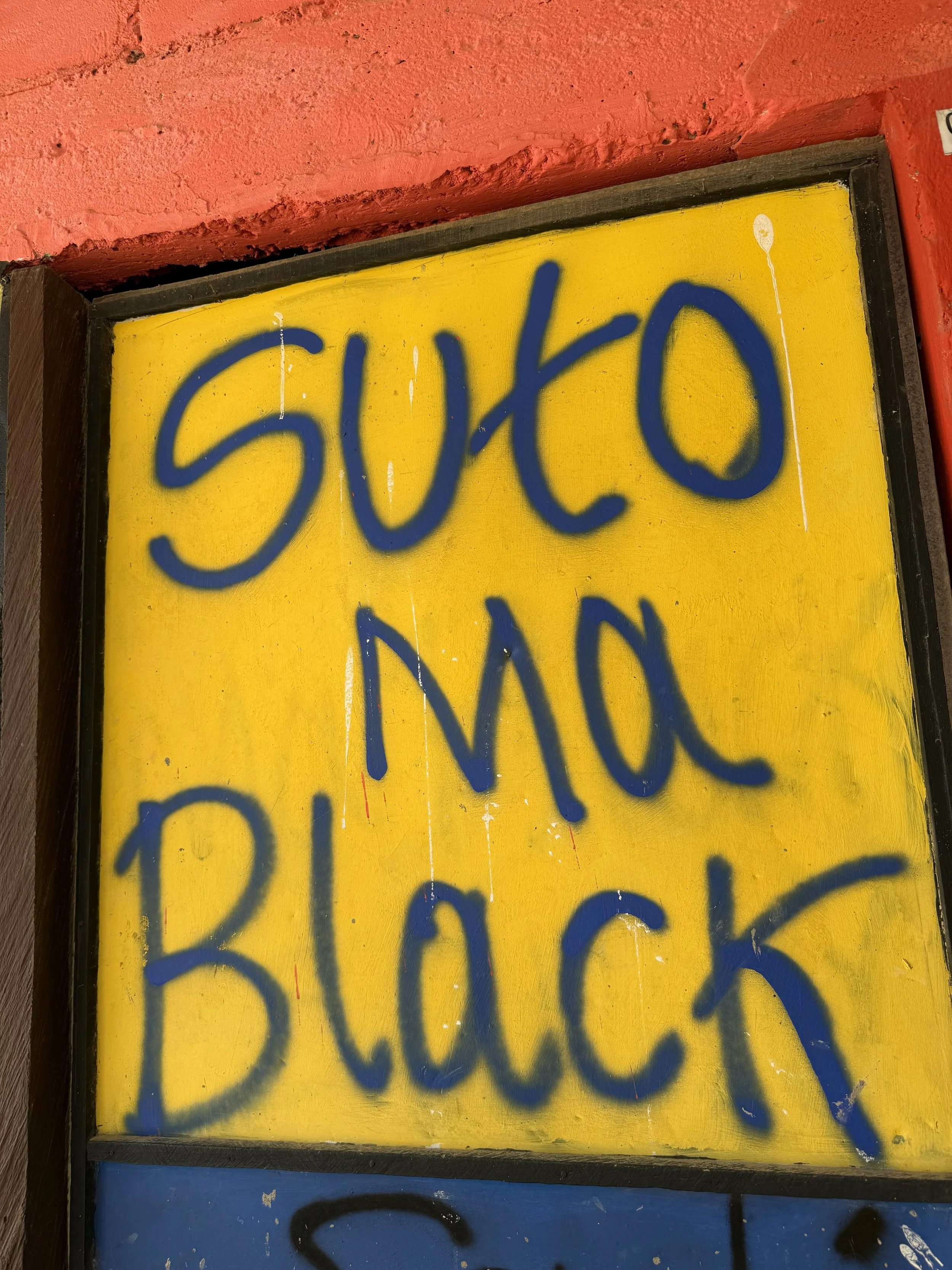 A yellow sign with blue spray-painted text that reads 'SUTO MAX BLACK'.