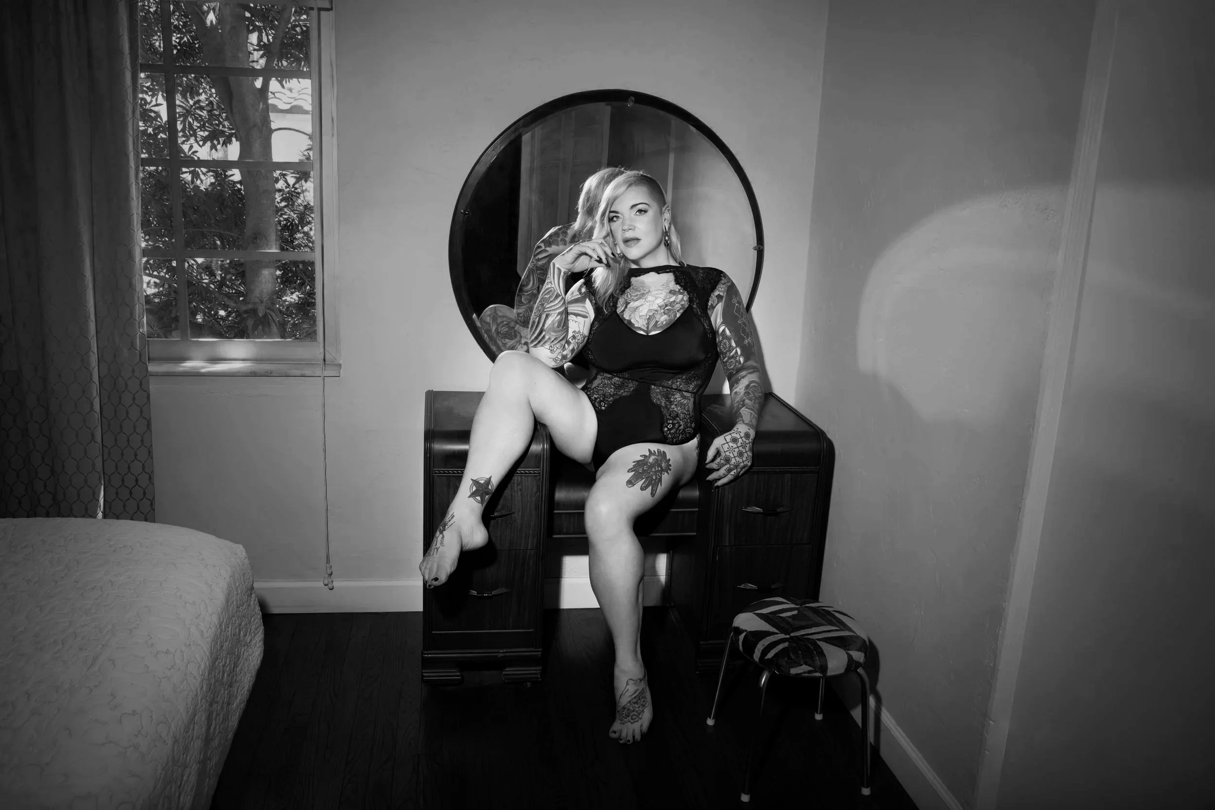 Chicago Prostate Massage Expert Erin Black wears a black lace bodysuit sitting on a vanity.