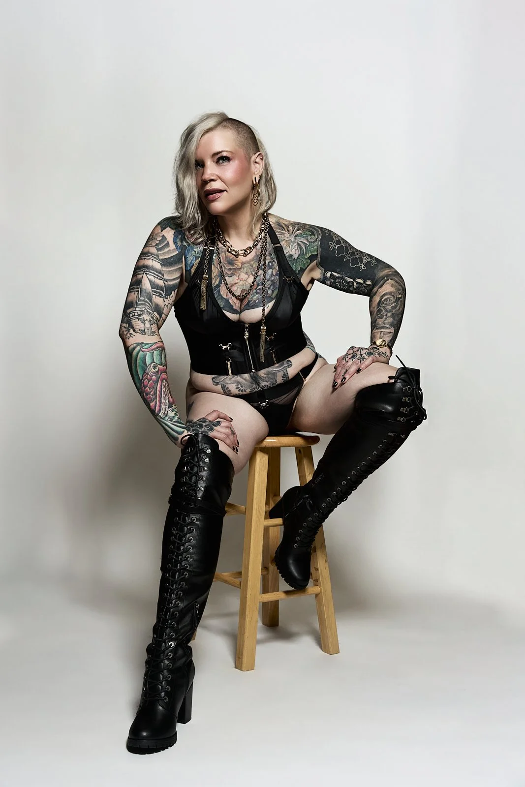 Chicago dominatrix Erin Black wears black satin lingerie and over the knee leather boots sitting on a stool.