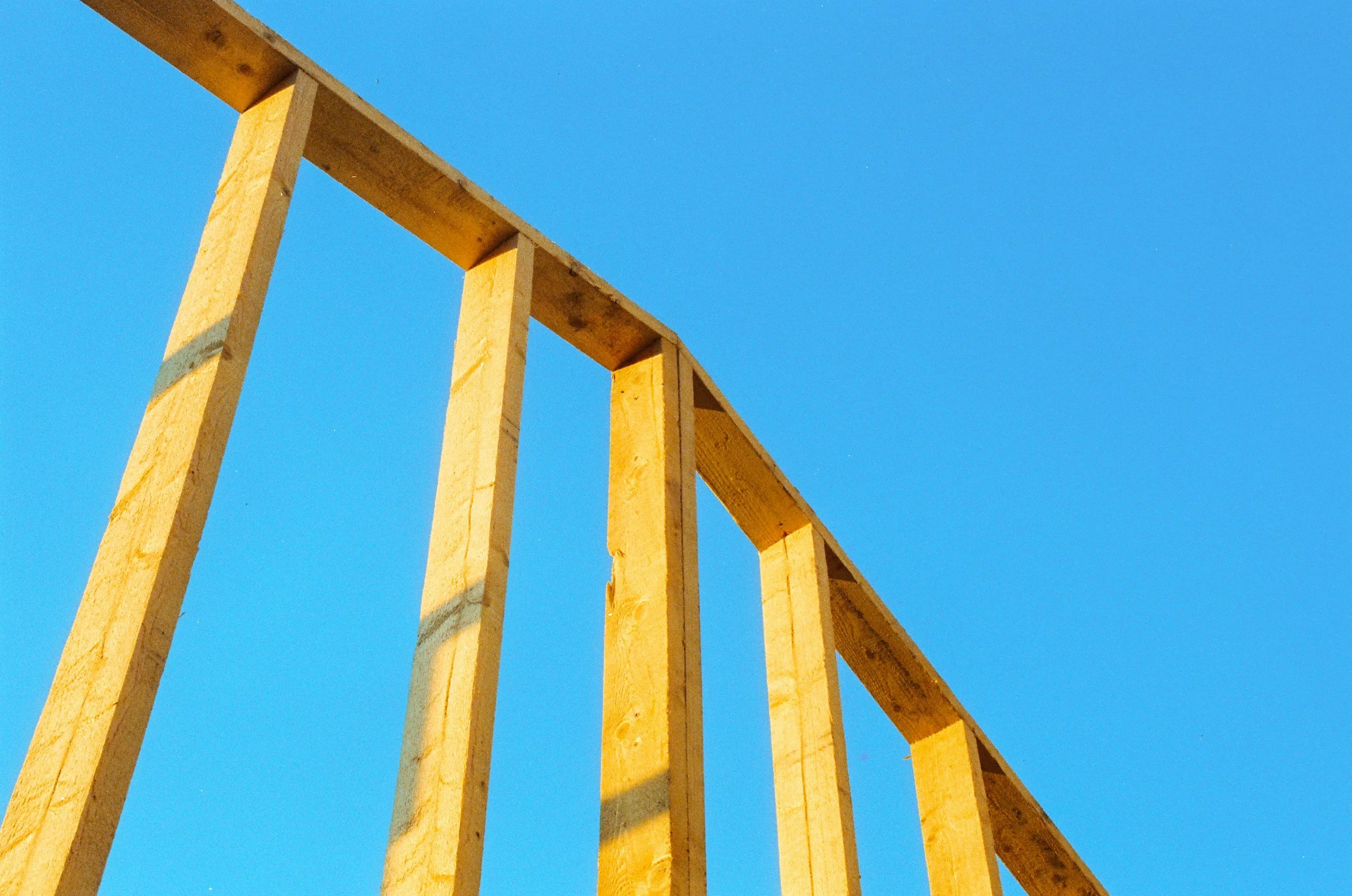 Wooden framing for a building under construction against a clear blue sky.