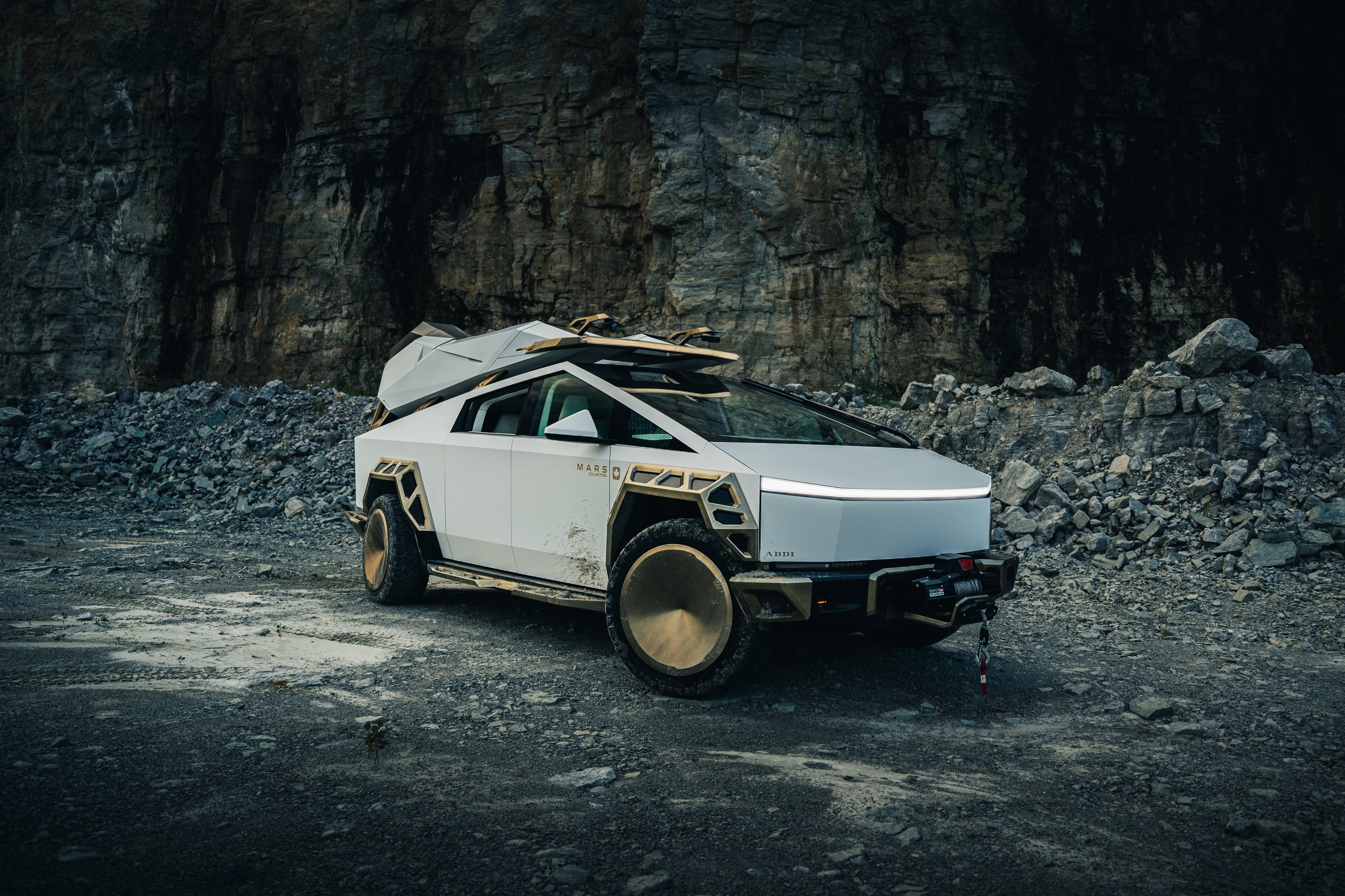 Futuristic white off-road vehicle with gold accents on a rocky terrain near a cliff.