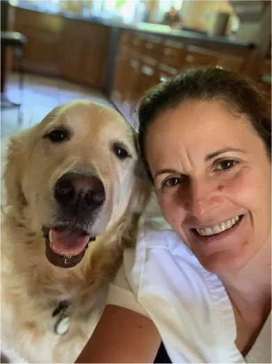 A woman smiling next to a large light-colored dog in a kitchen.