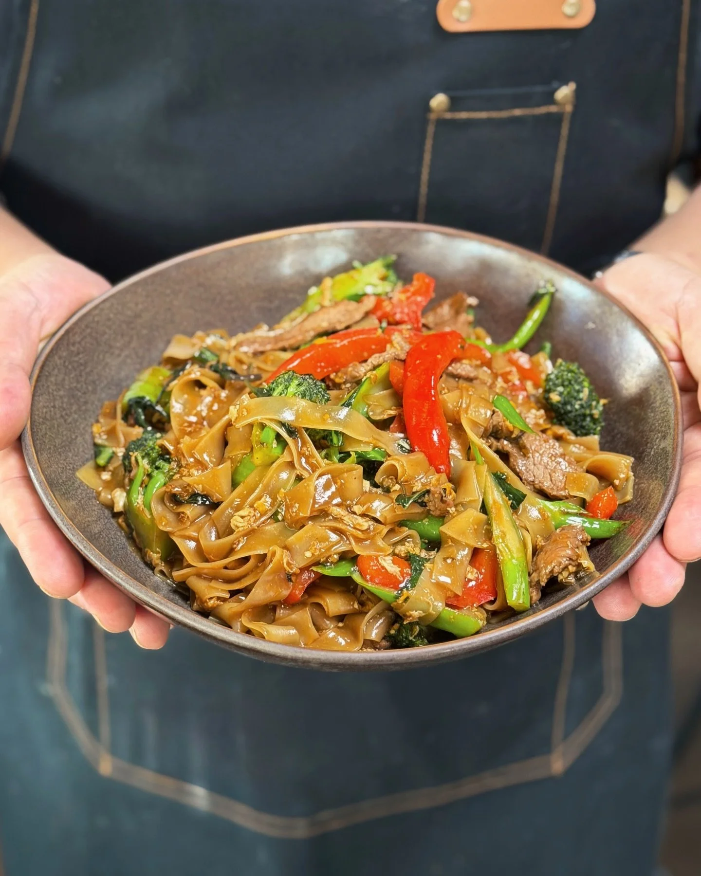 Pad Kee Mao, often called drunken noodles, is one of those dishes that tells a story with every bite. Rooted in Thai street food culture, it is bold, fast, and full of life. Wide rice noodles tossed over high heat with garlic, chili, Thai basil, and 