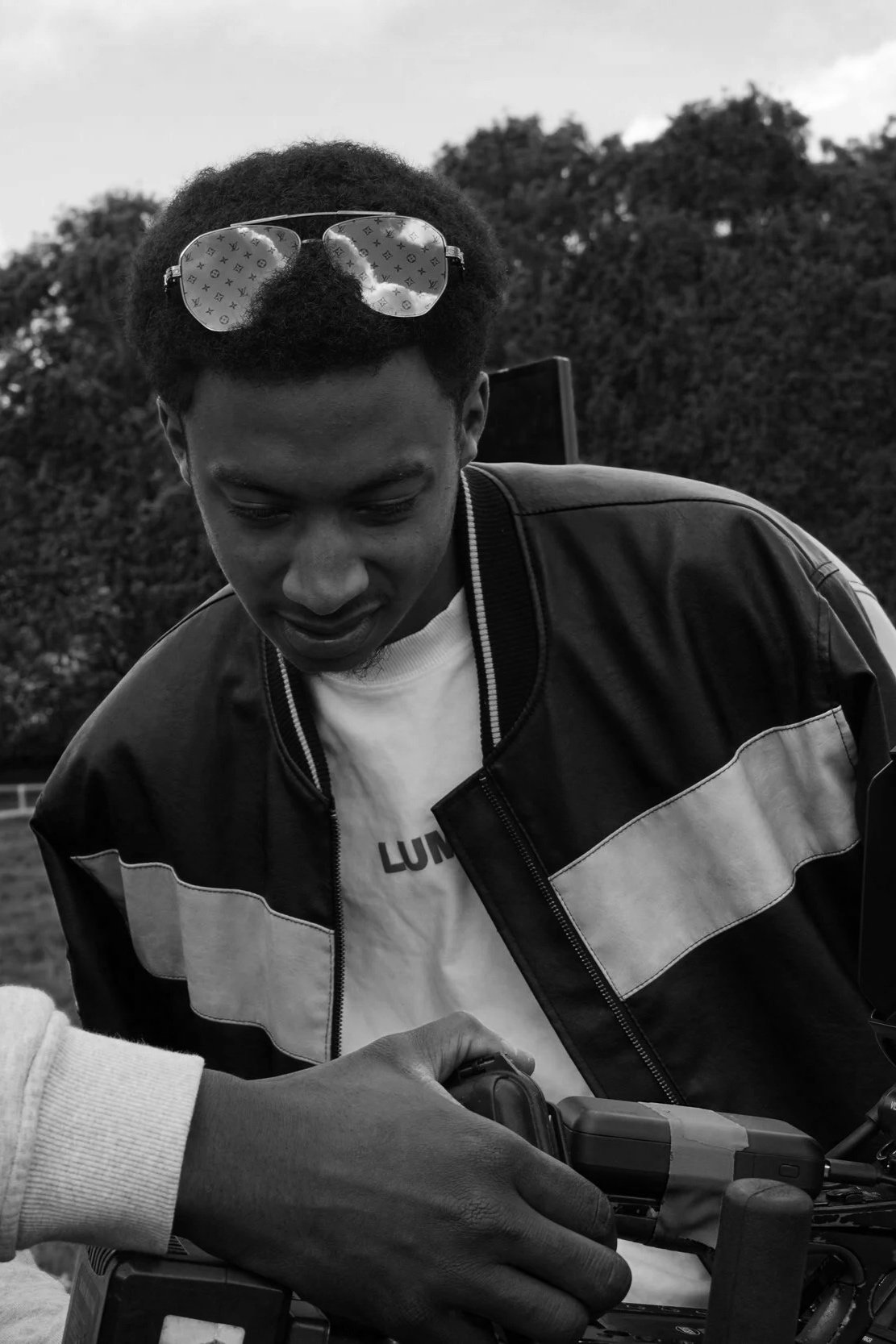 A young man with sunglasses on his head looking down at a device in someone else's hand outdoors.