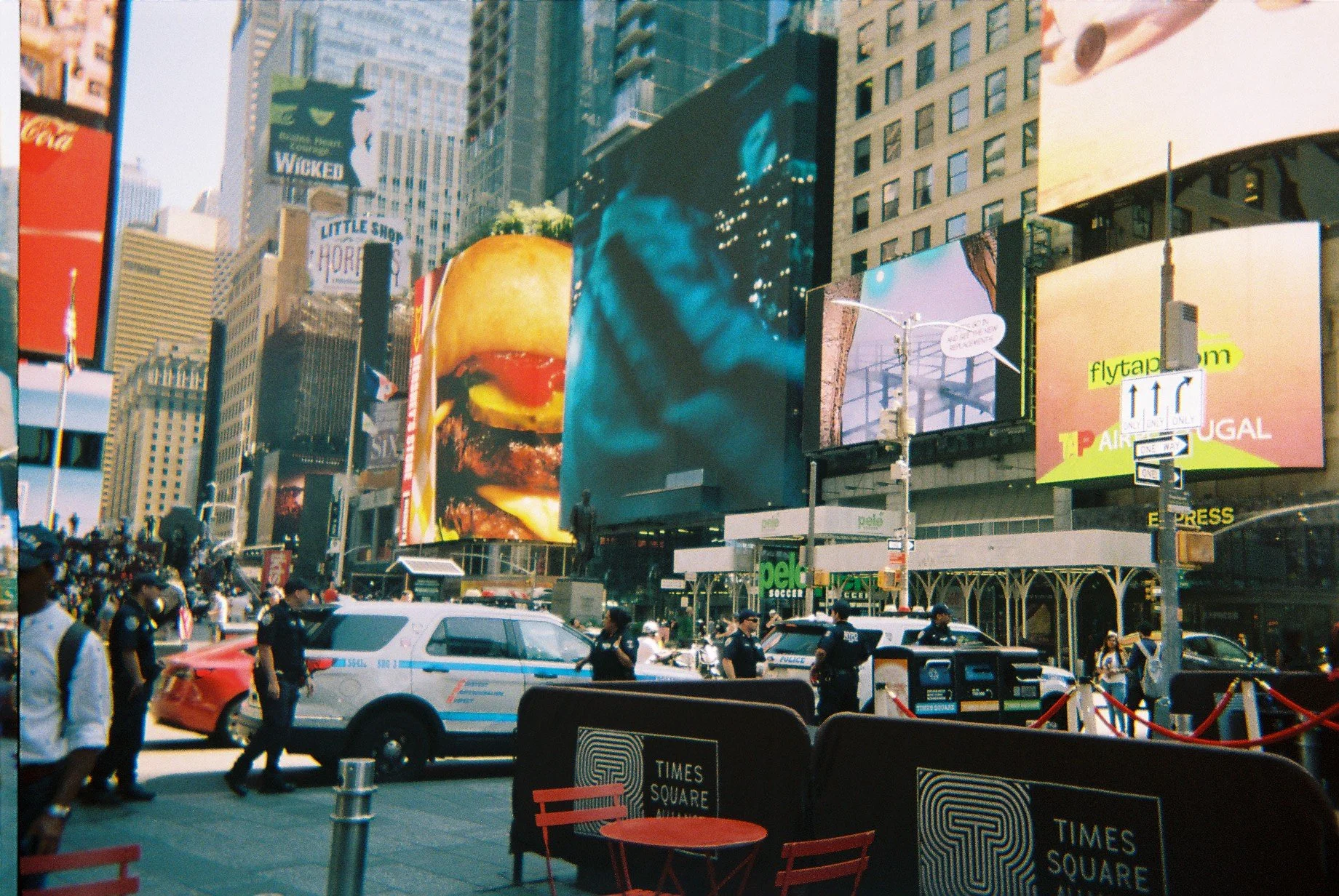 Busy Times Square in New York City with police officers, cars, and bright digital billboards advertising food, entertainment, and various brands.
